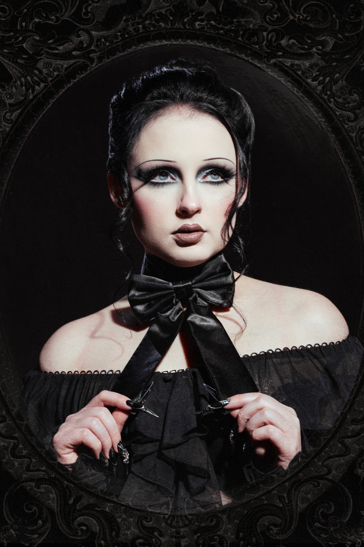 woman photographed against an ornate framed black background with her hair up wearing a black neck tie