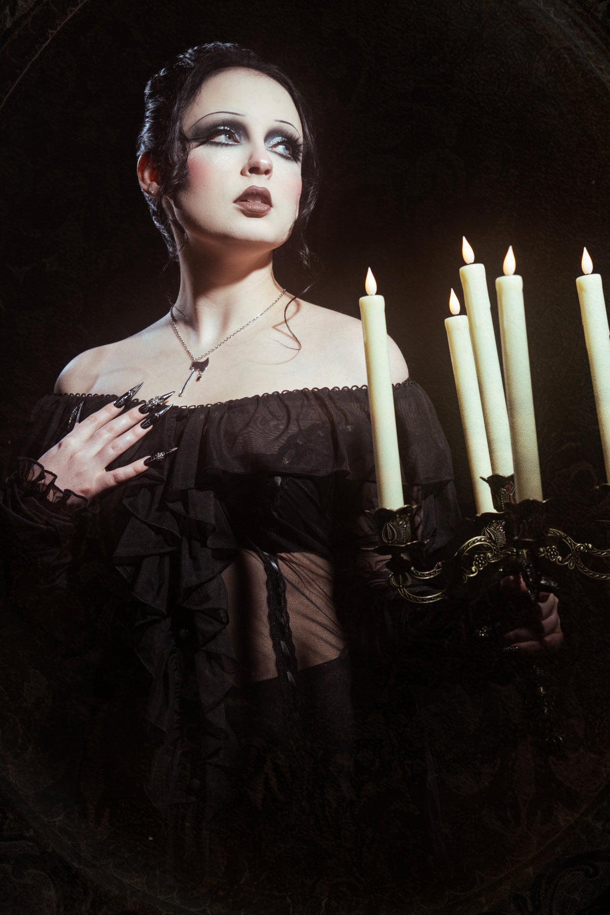 woman wearing a black off the shoulder dress holding a candelabra with white candles