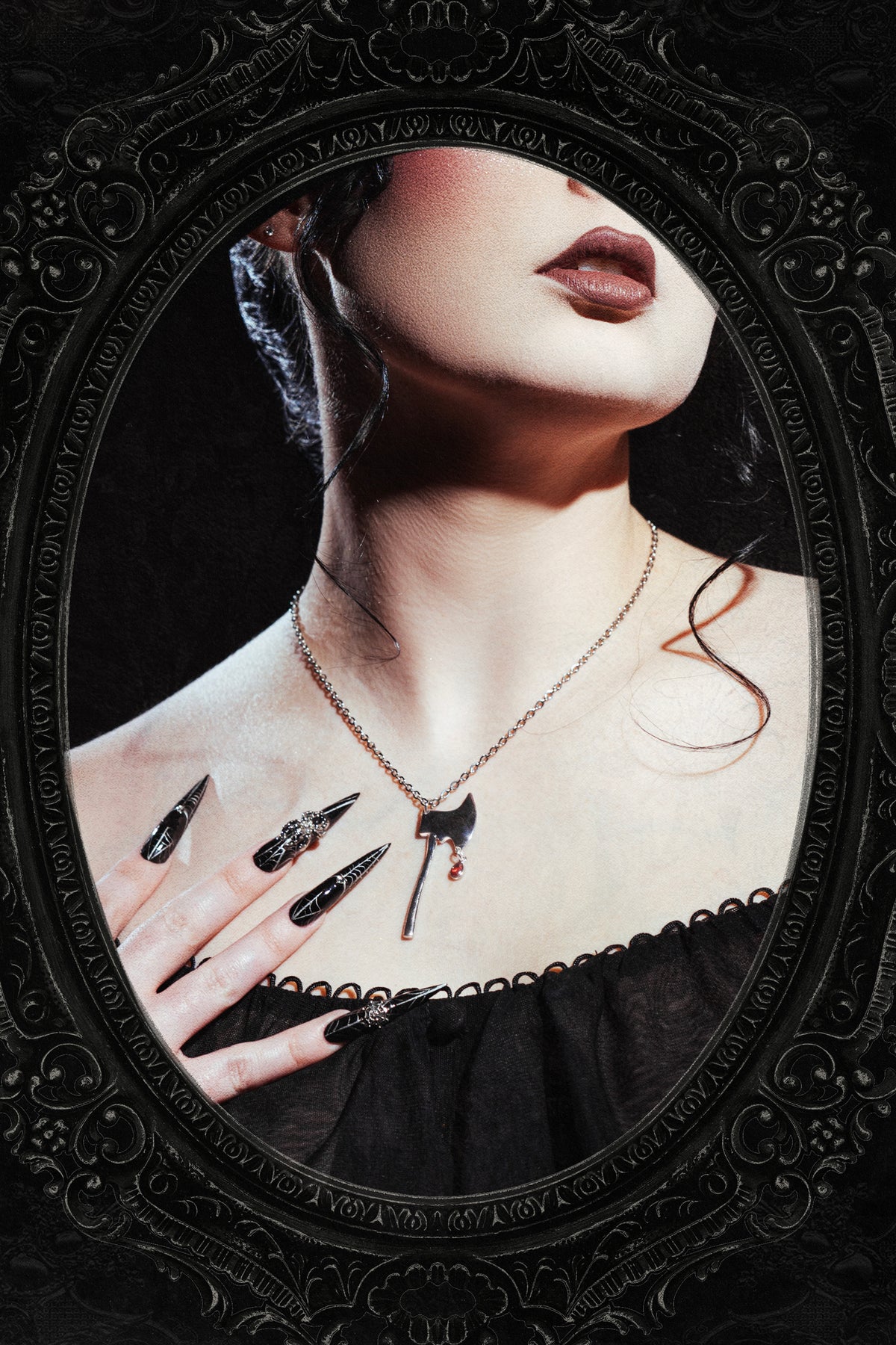 A gothic-style portrait of a woman with dark hair, wearing a delicate gold necklace with a miniature axe pendant and long black stiletto nails, framed within an ornate oval mirror.