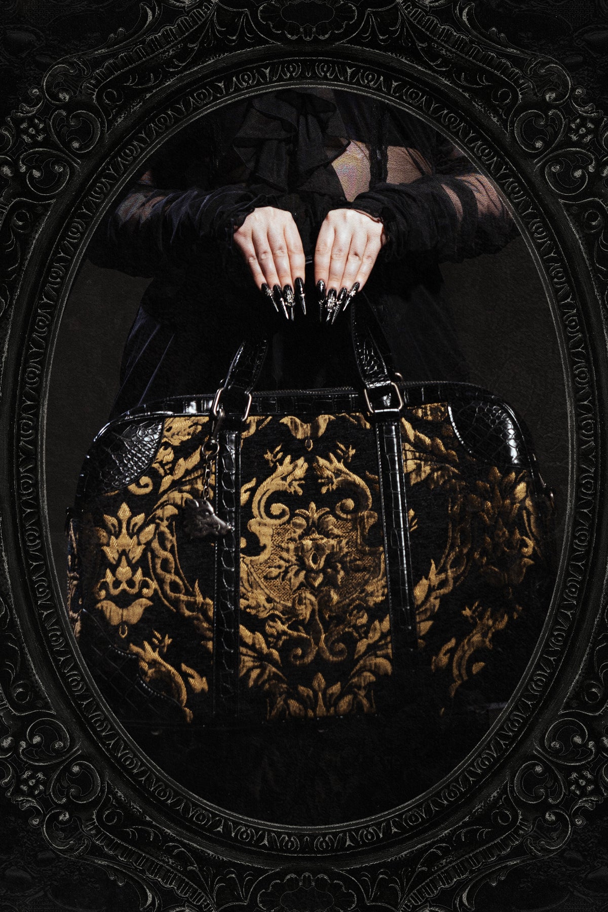 close up of hands holding a black and gold carpet bag with damask pattern