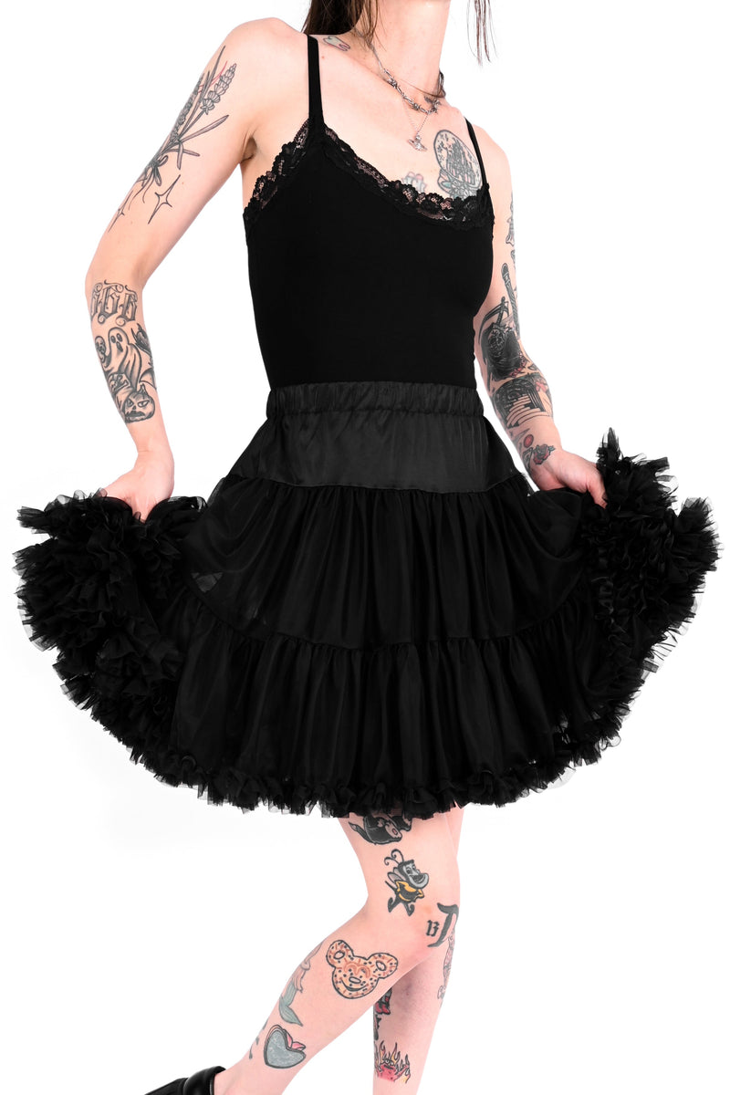 Person wearing a black tutu with tattoos on arms and legs against a white background