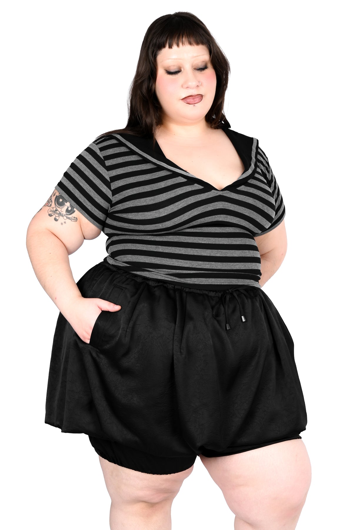 A plus-size model wearing a black and gray striped short-sleeve top with a V-neck and black shorts, standing against a plain white background.