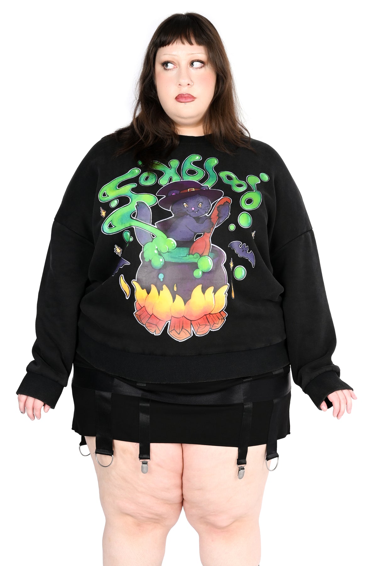 A model wearing a black crewneck sweatshirt with a colorful cat and cauldron graphic, styled with black garter shorts against a white background.