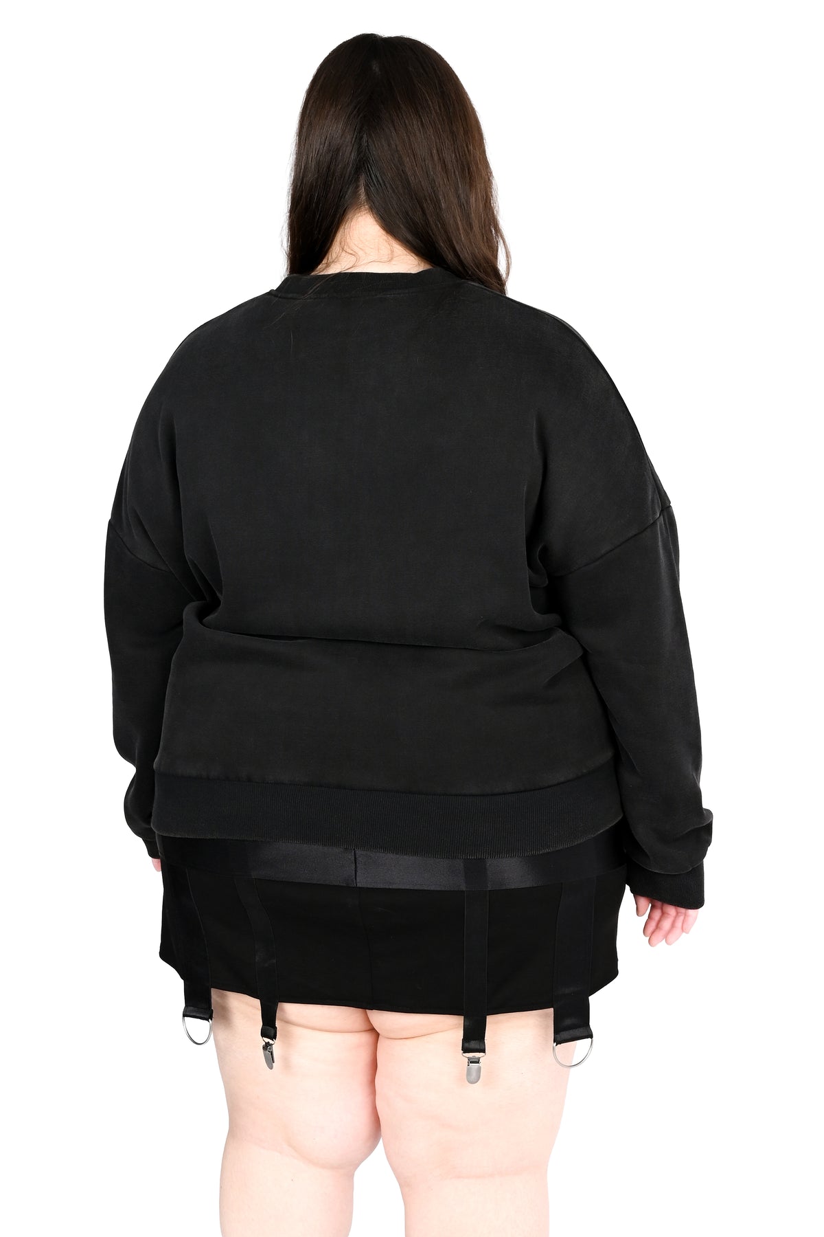 A person shown from the back wearing a black oversized long-sleeve top with a draped, layered hem and black garter-style shorts with metal clips, against a plain white background.