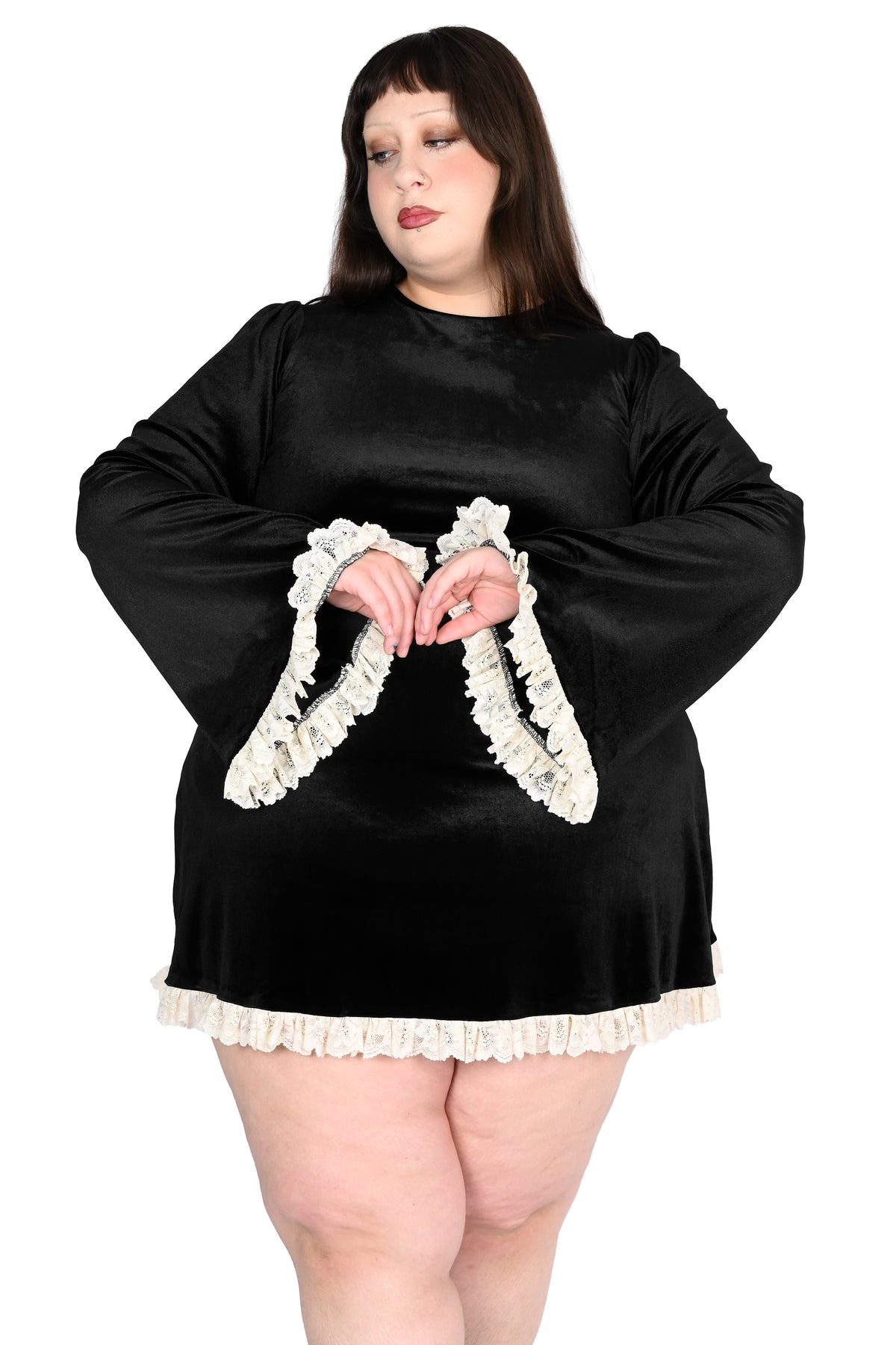 A plus-size model wearing a black long-sleeve dress with white ruffled trim on the cuffs and hem, posed against a solid white background.