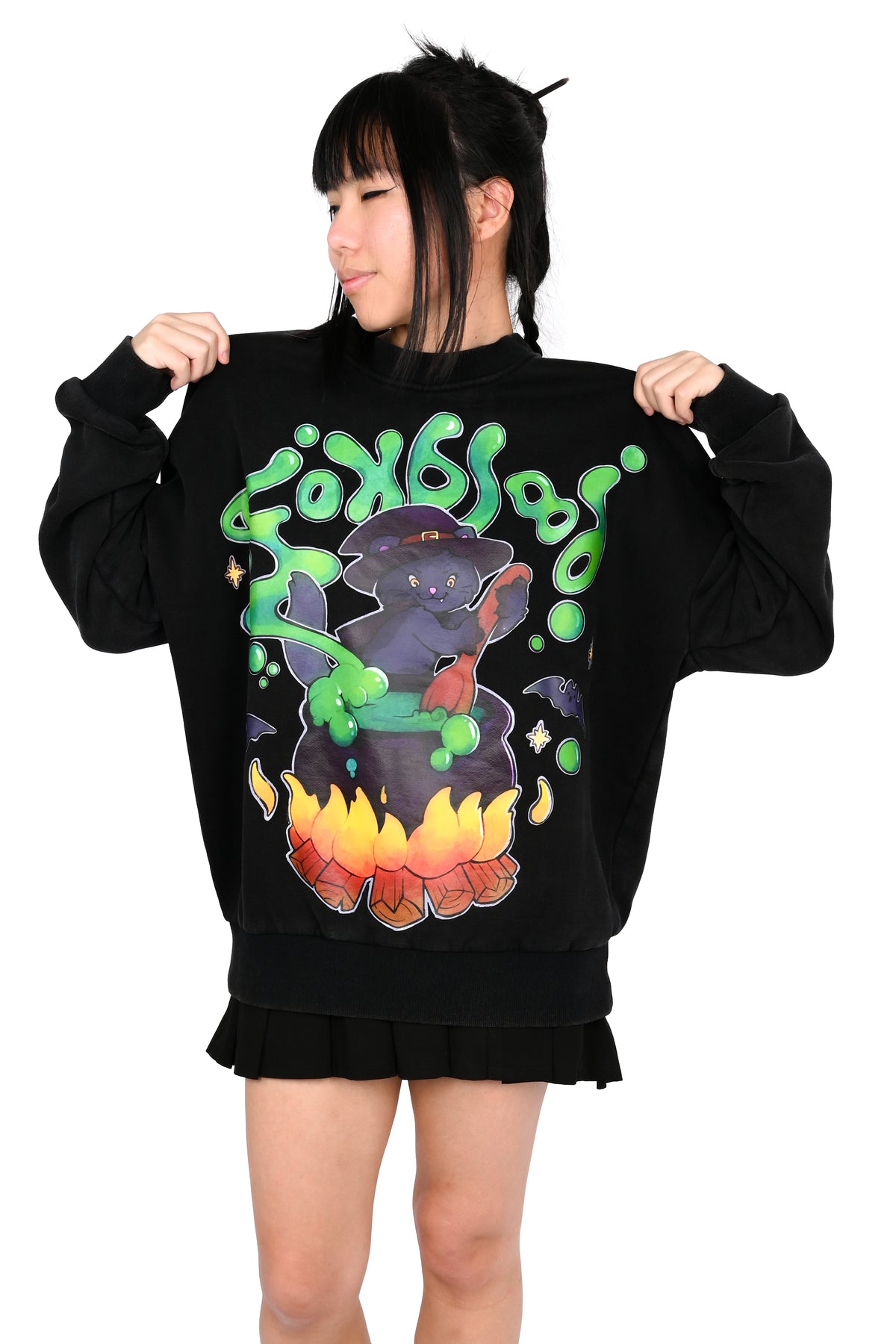 A model wearing a black sweatshirt with a large graphic of a dark cat in a cauldron with green slime and flames, set against a plain white background.