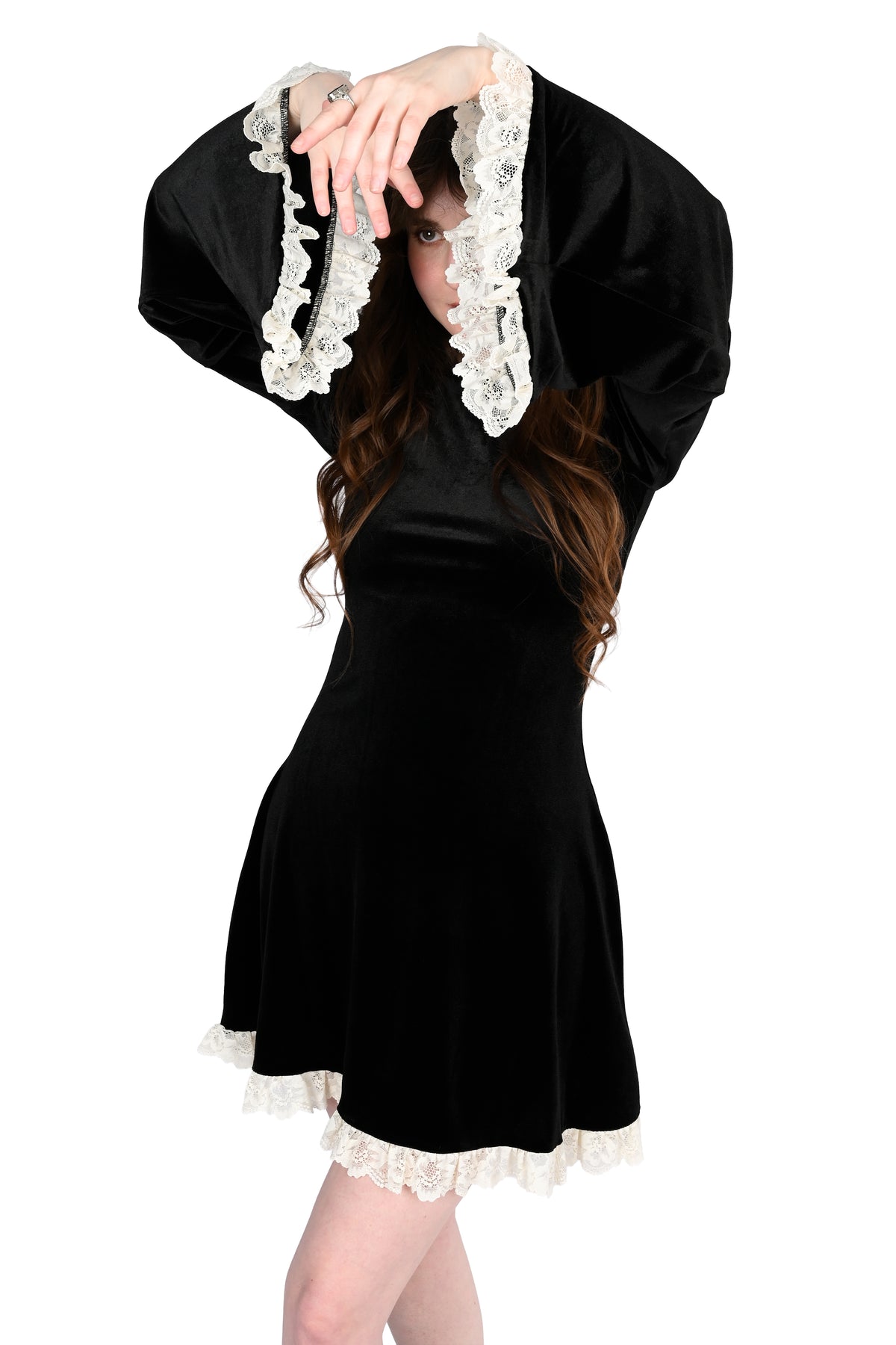 A woman modeling a black velvet dress with dramatic wide sleeves and white lace trim, posed against a plain white background.