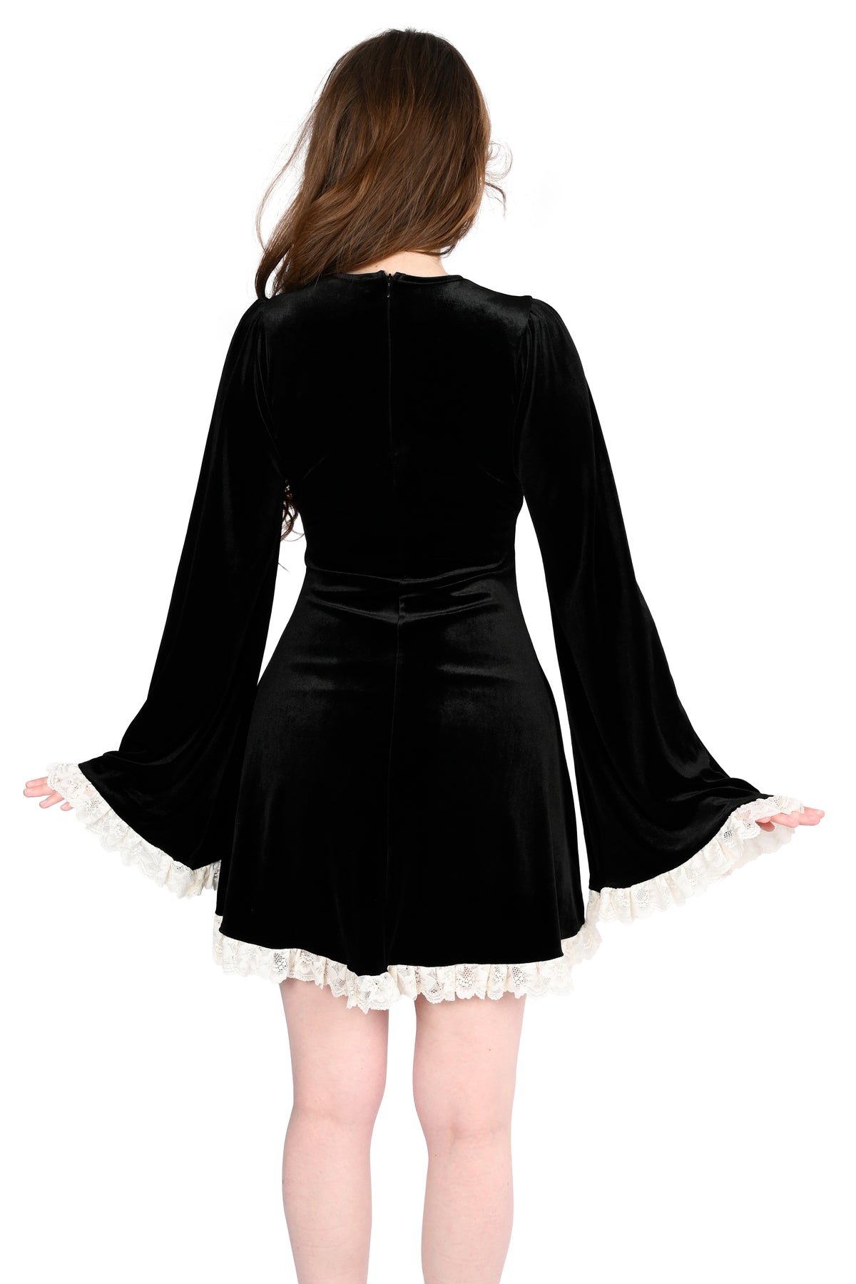 A woman shown from the back wearing a black velvet mini dress with long bell sleeves, white ruffled trim at the cuffs and hem, and a matching black belt at the waist.
