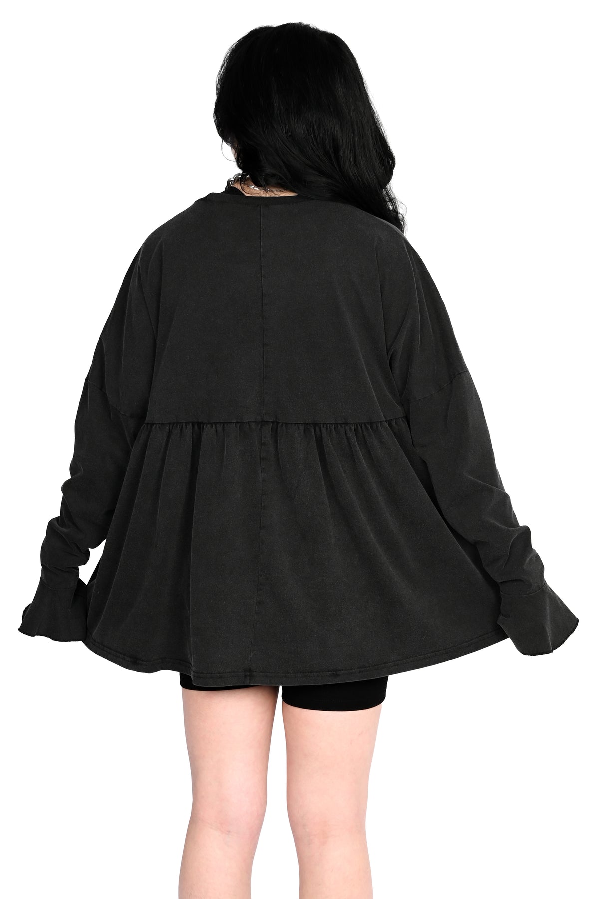 A person shown from the back wearing a loose black long-sleeve top with a gathered waist seam and flared cuffs, paired with black shorts, against a plain white background.