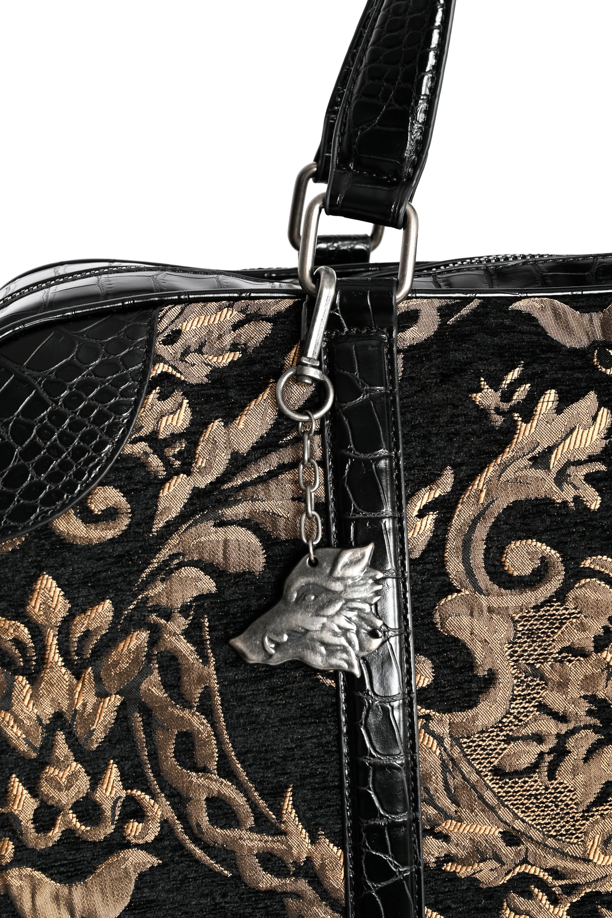 Close-up of a black and gold damask-patterned handbag with textured faux-croc and woven jacquard details, featuring a silver-tone boar head charm.