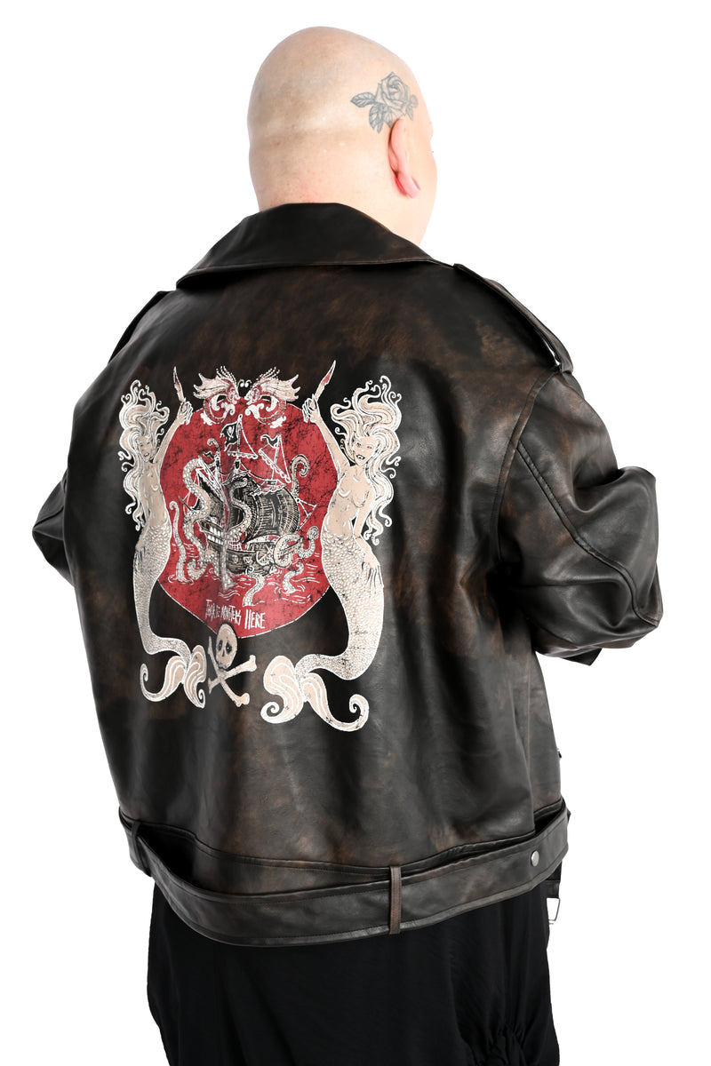 A model viewed from behind wearing a distressed black leather jacket with a large pirate themed graphic on the back, set against a plain white background. The graphic depicts two mermaids holding daggers on either side of a pirate ship that is being devoured by a kraken. There is a skull and crossbones under. The text 'there will be monsters' is visible