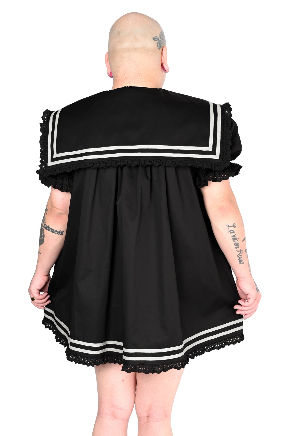 back view of a model wearing a black sailor dress with off-white stripe detailing and lace trim in size 2xl, holding each side of the dress