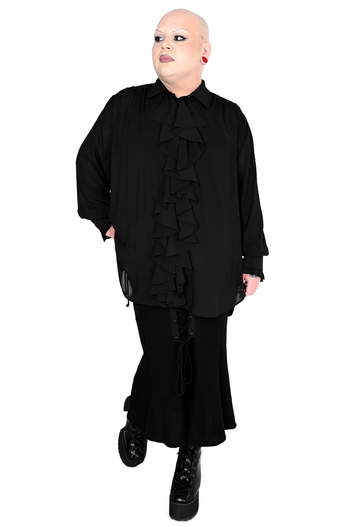 A person modeling a black long-sleeve blouse with dramatic front ruffles and a matching black skirt against a plain white background.
