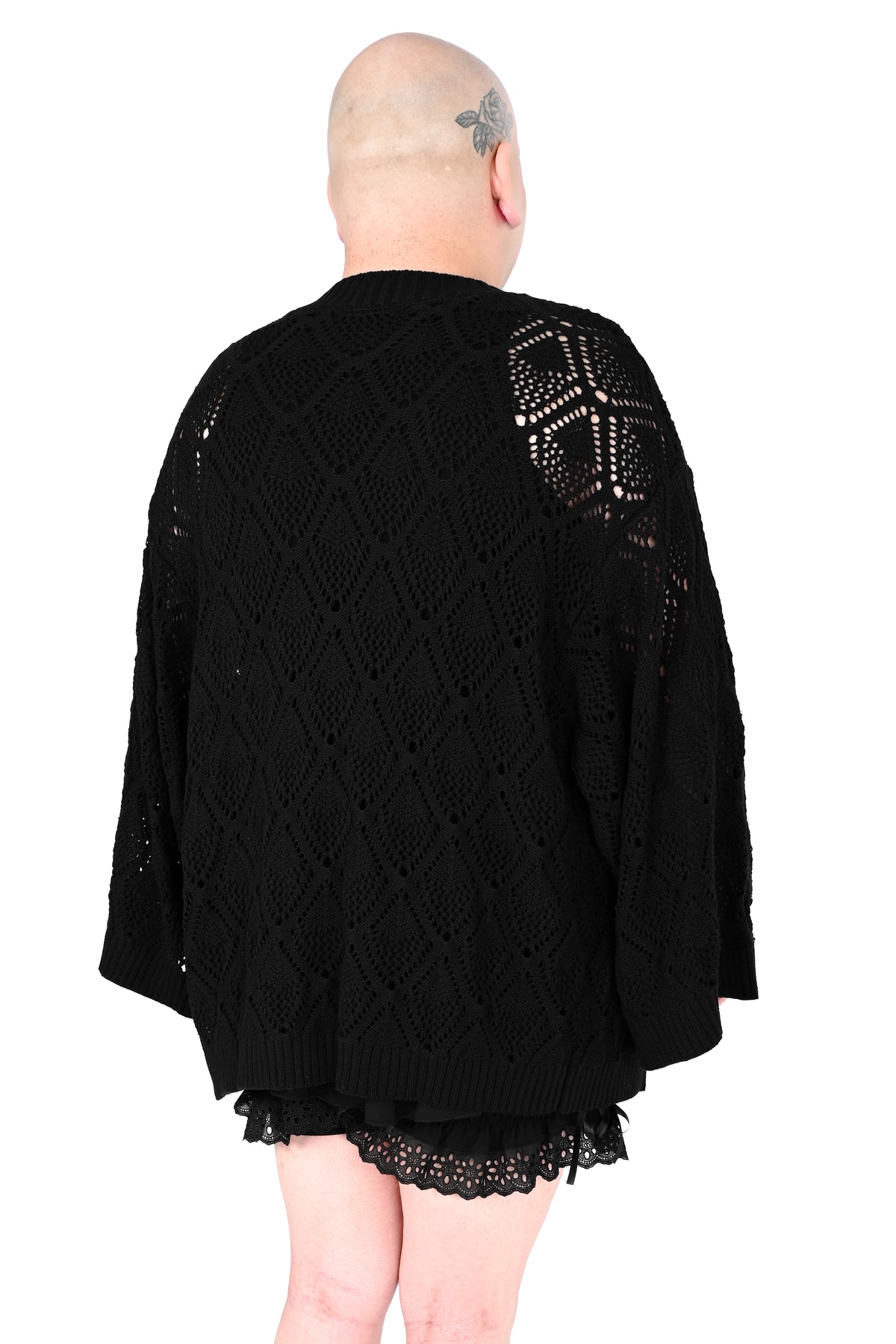 A person shown from the back wearing an oversized black open-knit cardigan with a geometric lace pattern on the upper back and shoulders, photographed against a plain white background.