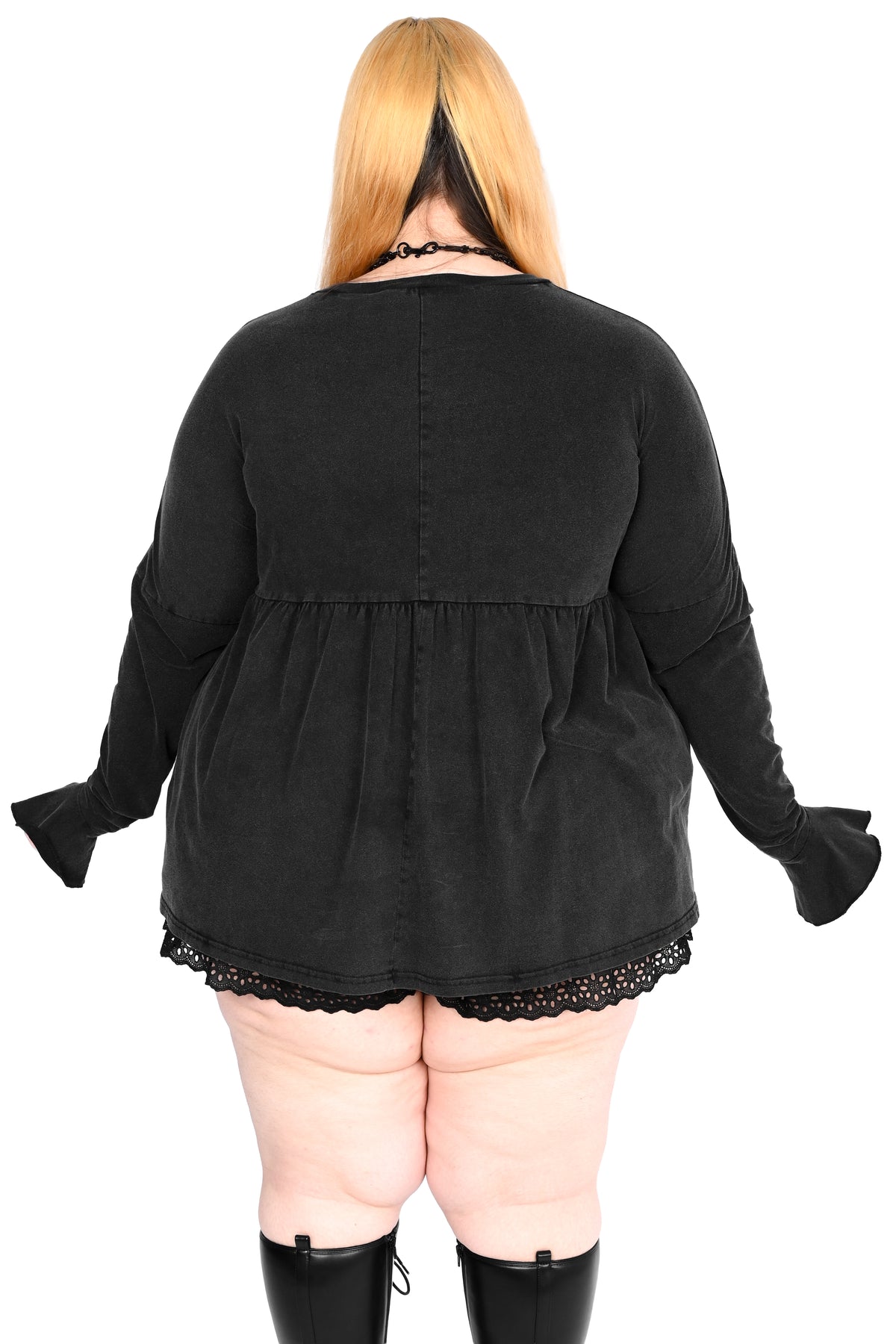 A plus-size model viewed from the back, wearing a black long-sleeve top with a gathered waist and lace hem, paired with black knee-high boots against a white background.