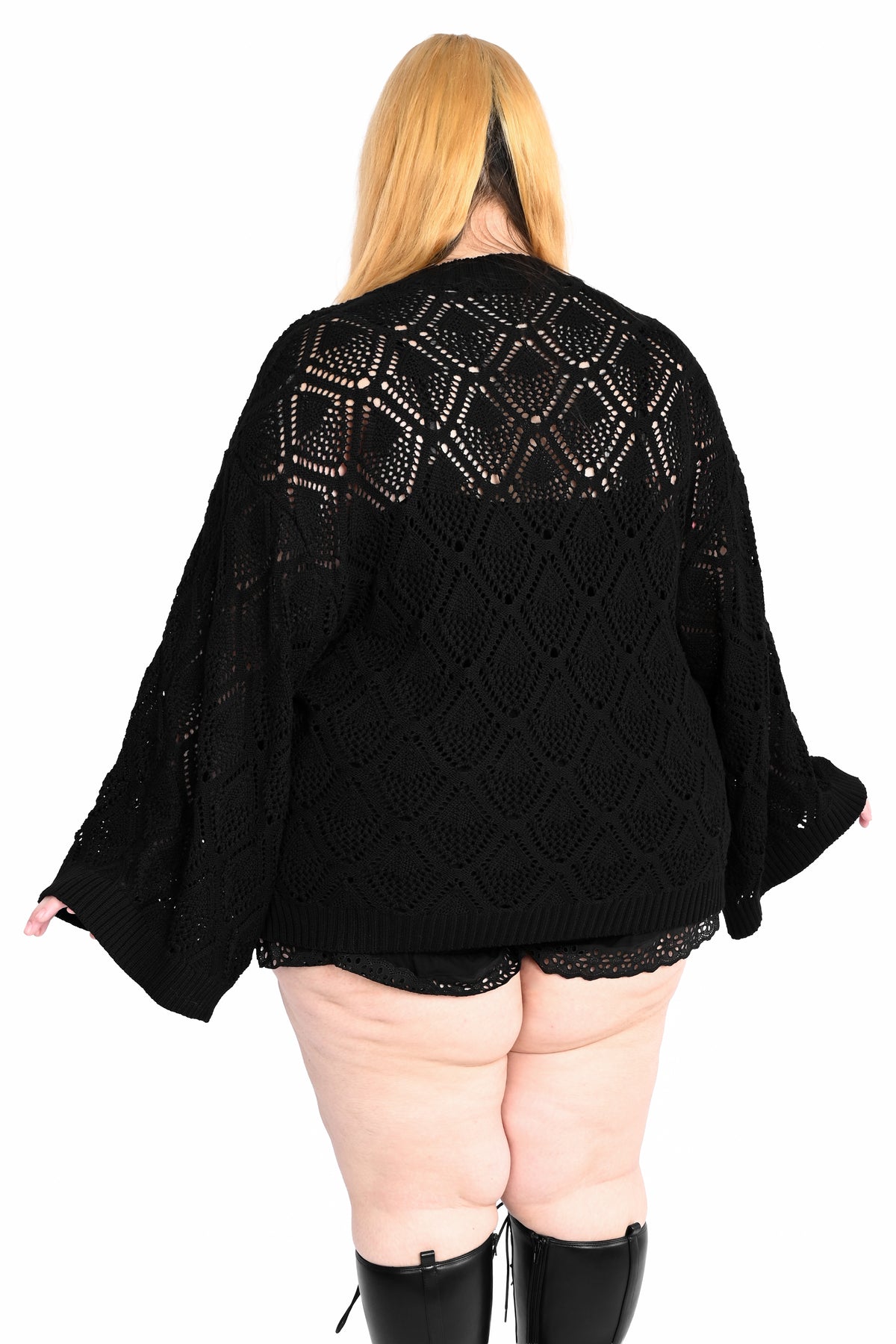 A person shown from the back wearing a black open-knit cardigan or poncho-style sweater with wide sleeves, photographed against a plain white studio background.