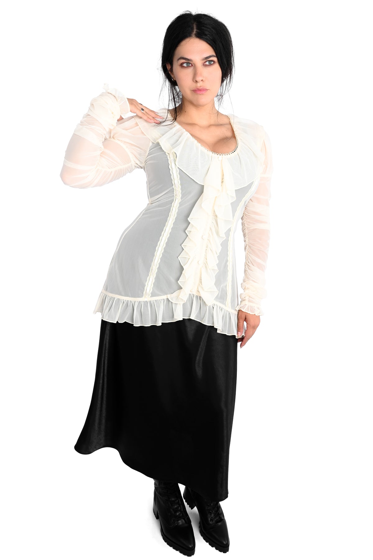 A woman modeling a white ruffled long-sleeve blouse with sheer sleeves and a black midi skirt, photographed against a plain white background.