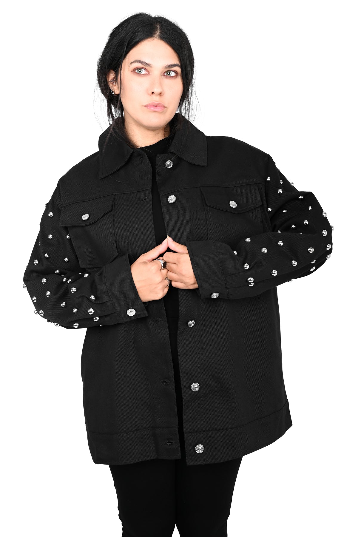 A woman modeling a black button-up jacket with silver studs on the sleeves, photographed against a plain white background.