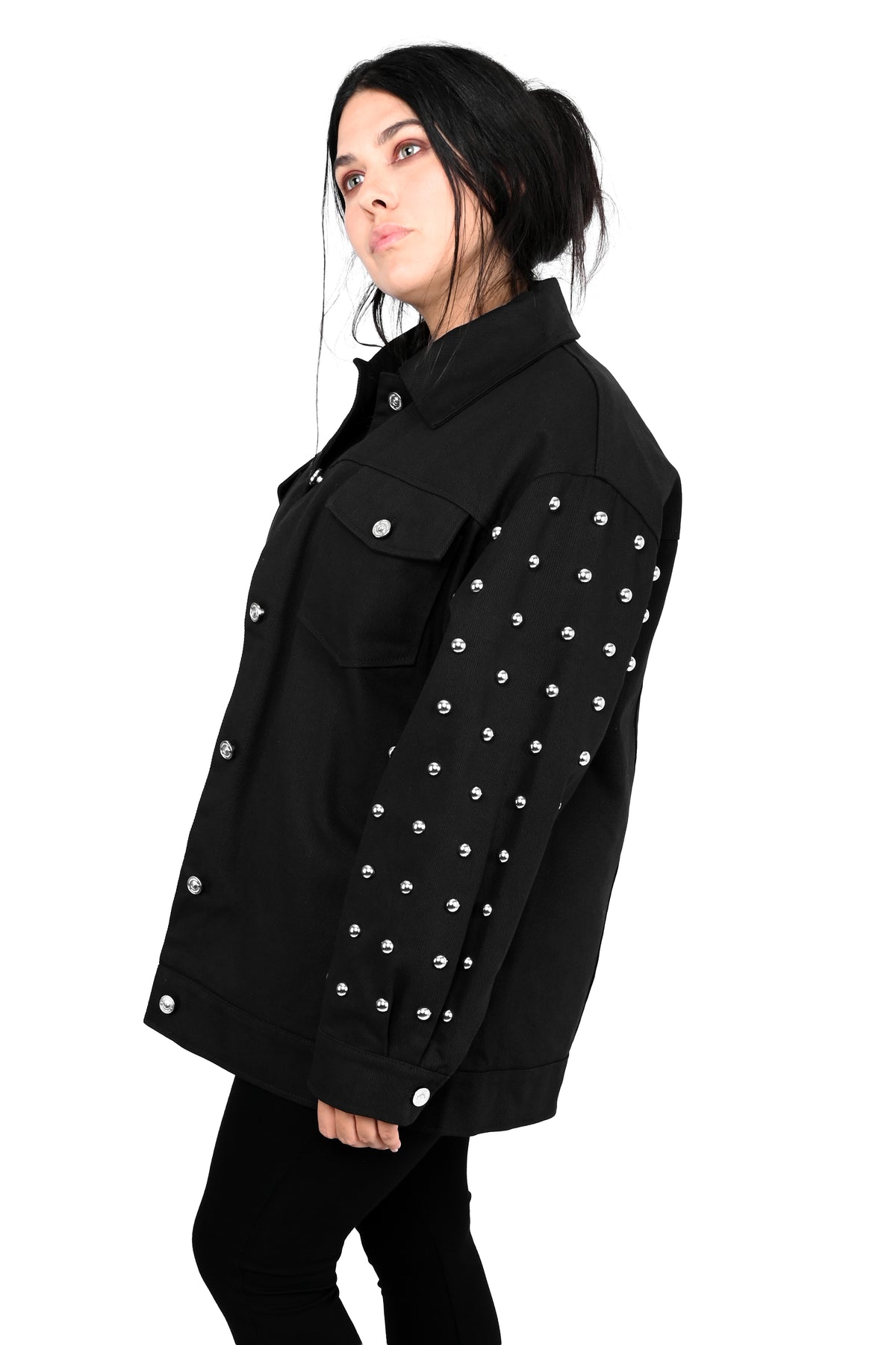 A woman wearing a black denim-style jacket with silver studs on the sleeves and front, shown in profile against a plain white background.