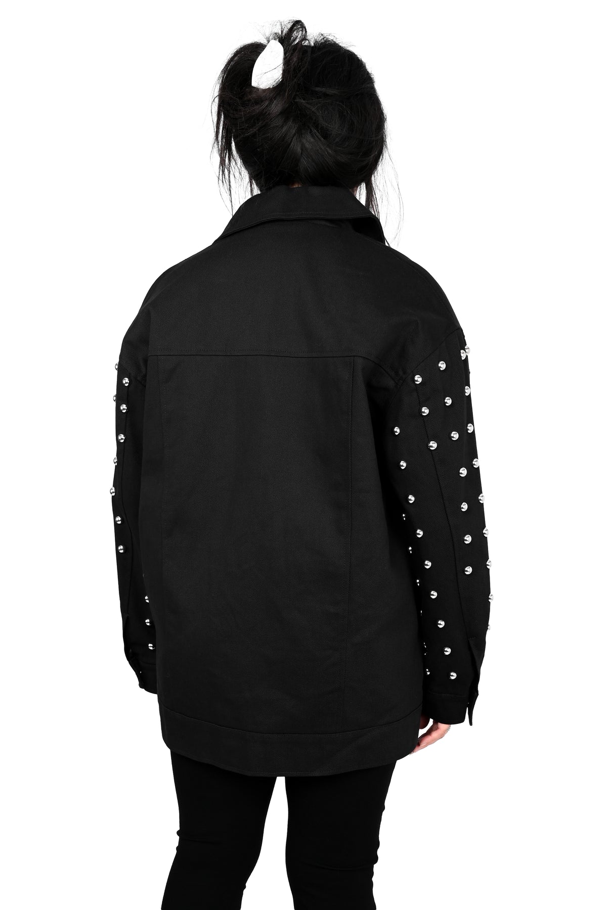 A person shown from the back wearing a black jacket with silver studs down both sleeves, paired with black pants, against a plain white background.