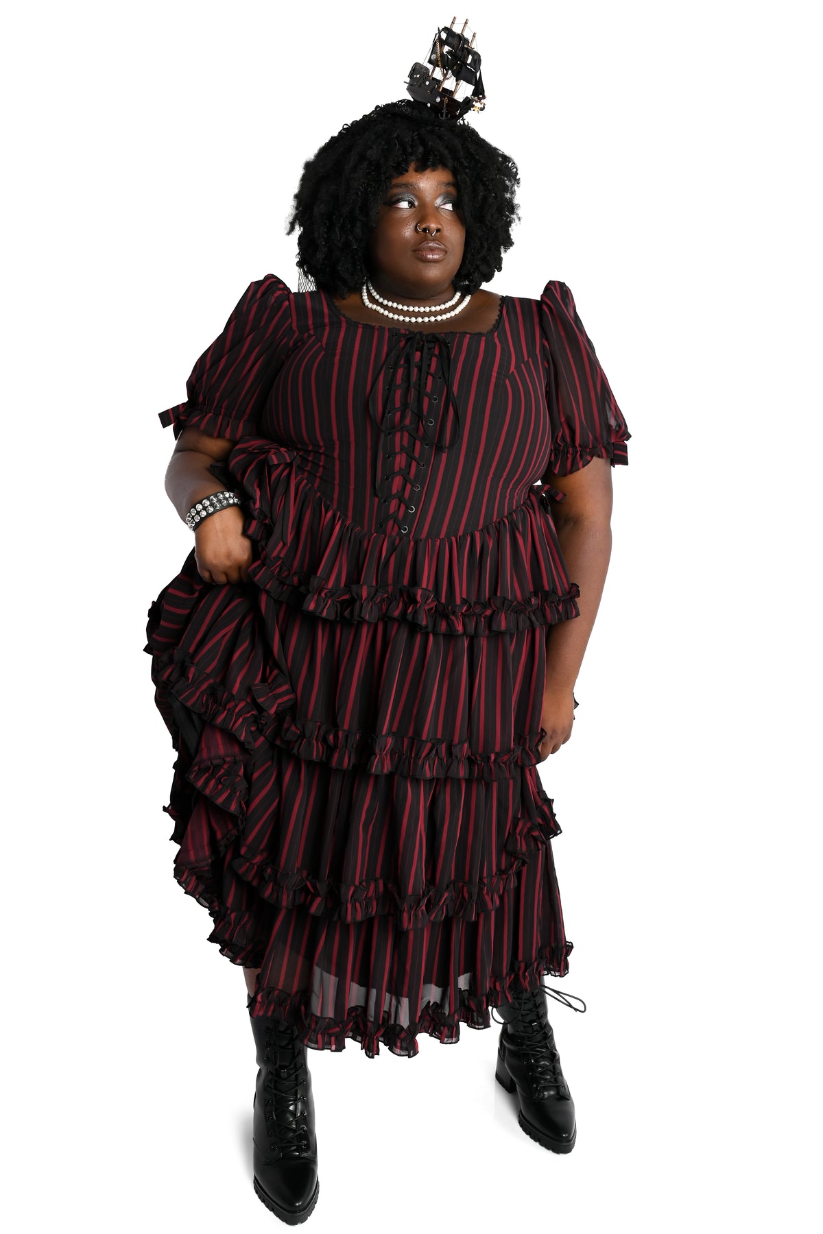 A woman modeling a black and red vertically striped ruffled dress with puff sleeves, lace-up front, and black lace-up boots against a plain white background.