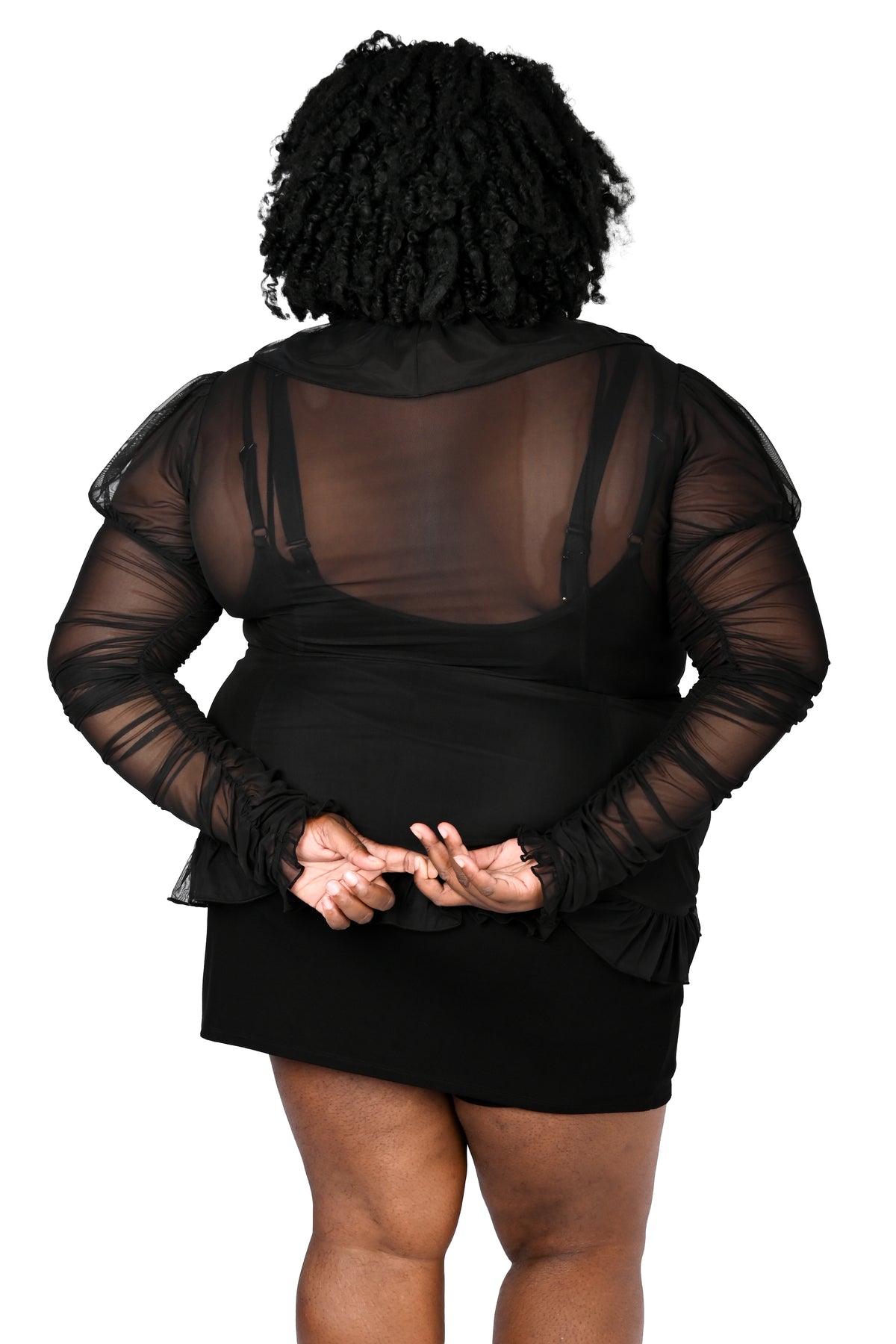 A person shown from the back wearing a black sheer long-sleeve top over a black dress, against a plain white background.