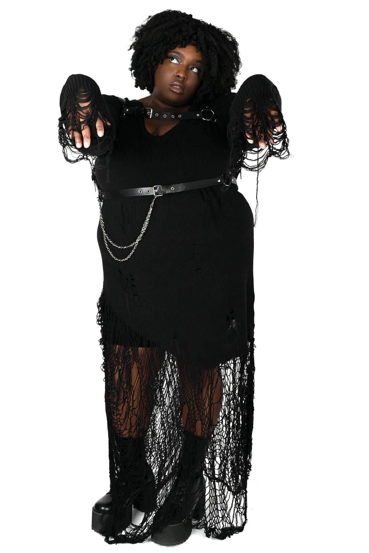 A model wearing a gothic black distressed maxi dress with sheer hem, a black belt with silver chain accents, and a black choker, posed with her hands out against a solid white background.