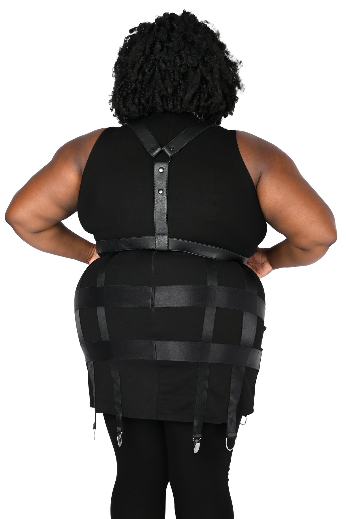 A person shown from the back wearing a black harness with a fitted sleeveless top and black leggings, photographed against a plain white studio background.