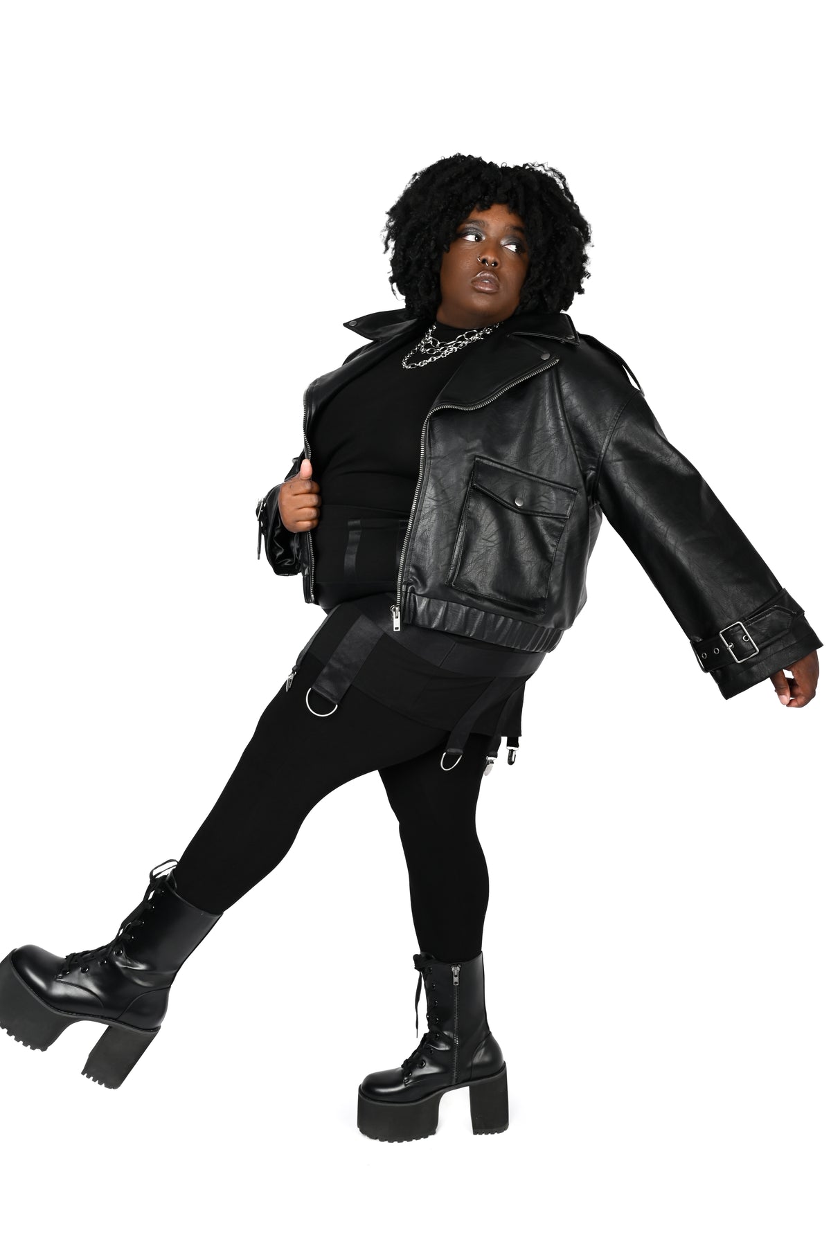 A person modeling a black faux-leather moto jacket, black outfit, and chunky black platform boots against a plain white background.