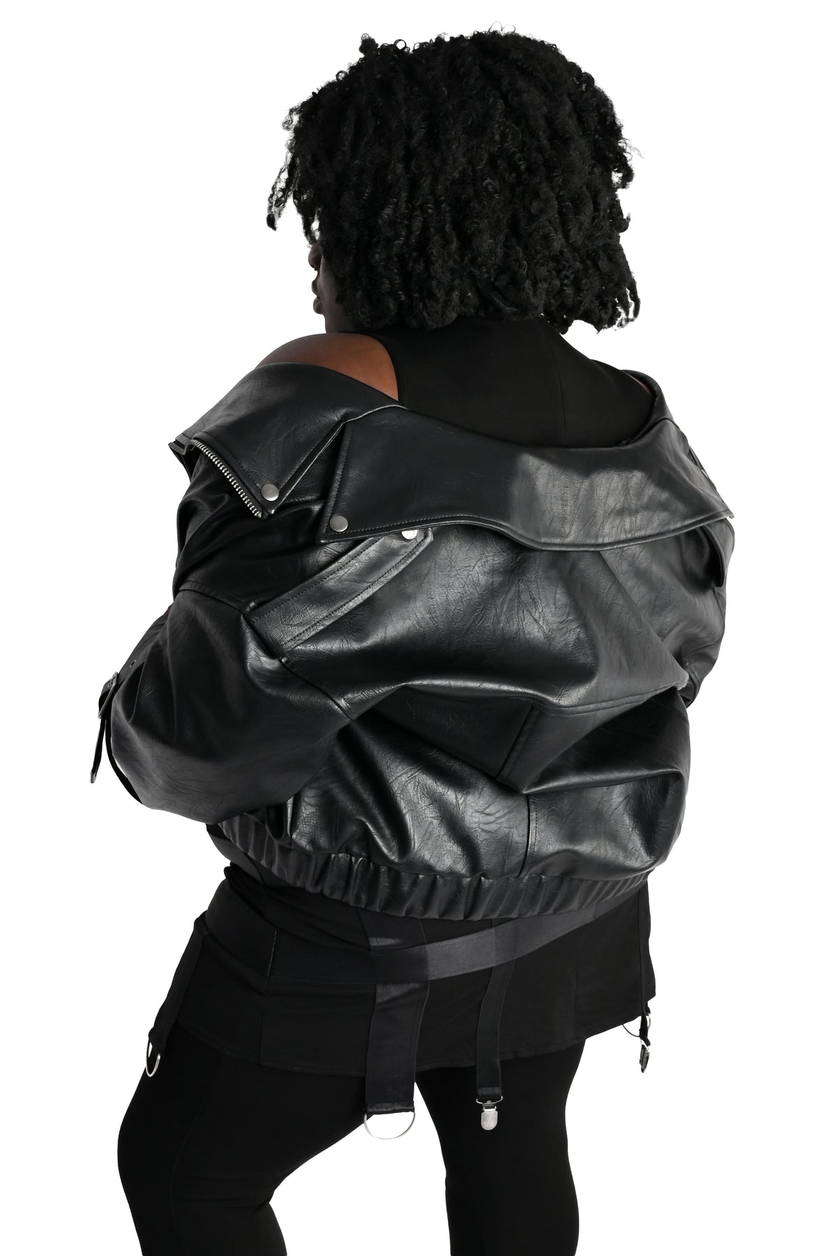 A person shown from the back wearing a black faux-leather jacket with a gathered elastic hem, paired with black pants, against a plain white background.