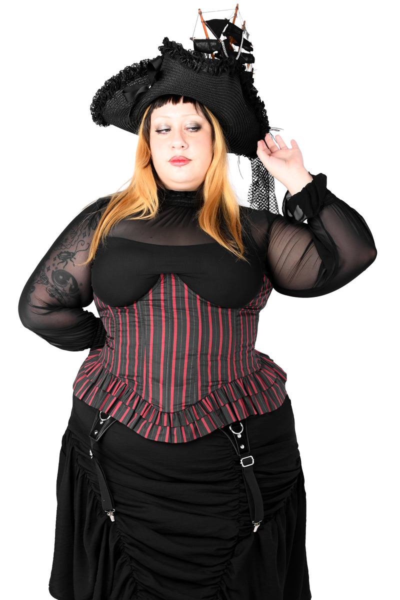 A woman modeling a black pirate costume with a striped corset top, sheer black sleeves, a black skirt, and a black pirate hat with a small ship decoration, against a plain white background.