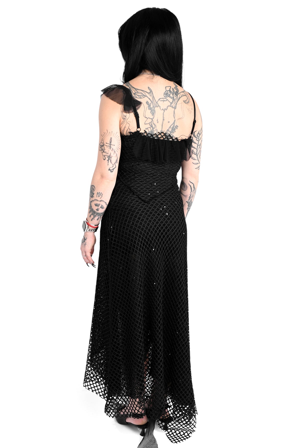 A woman viewed from the back wearing a long black fishnet maxi dress with ruffled straps and a ruffled waist, photographed against a plain white background.