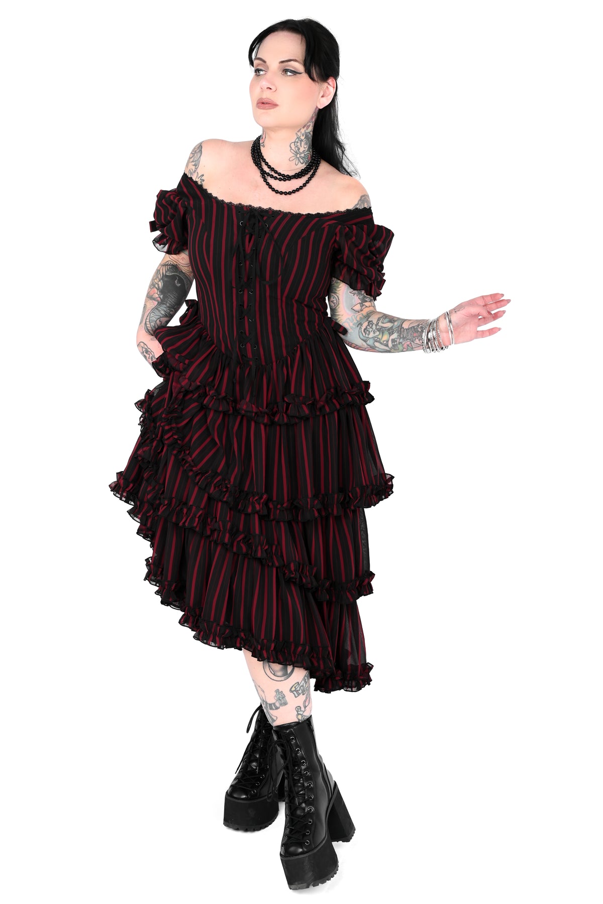 A model wearing a black and red vertically striped off-the-shoulder ruffled dress with black platform combat boots, set against a plain white background.