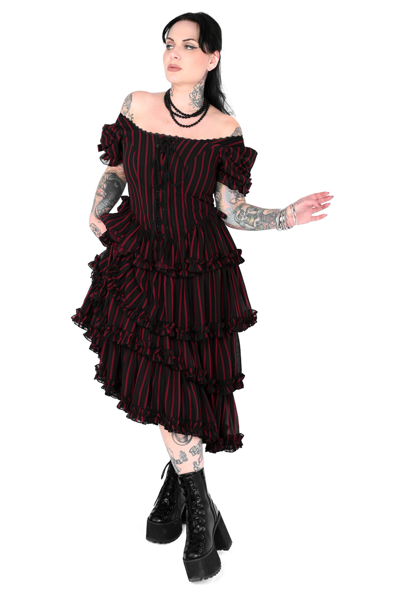 A model wearing a black and red vertically striped off-the-shoulder ruffled dress with black platform combat boots, set against a plain white background.