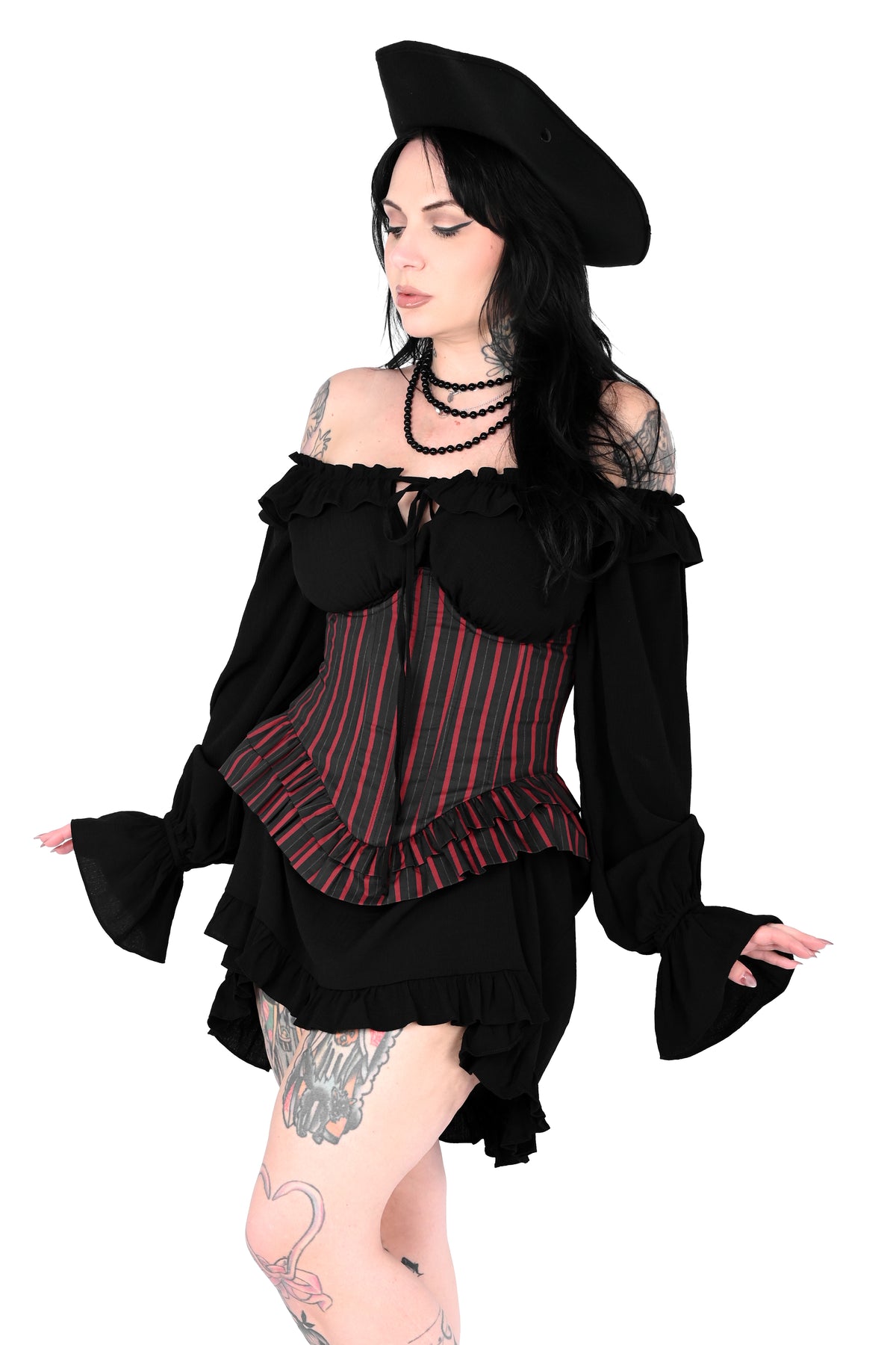 A model wearing a black gothic-style outfit with a red and black striped corset, a matching black beret, and a ruffled black dress, posed against a solid white background.