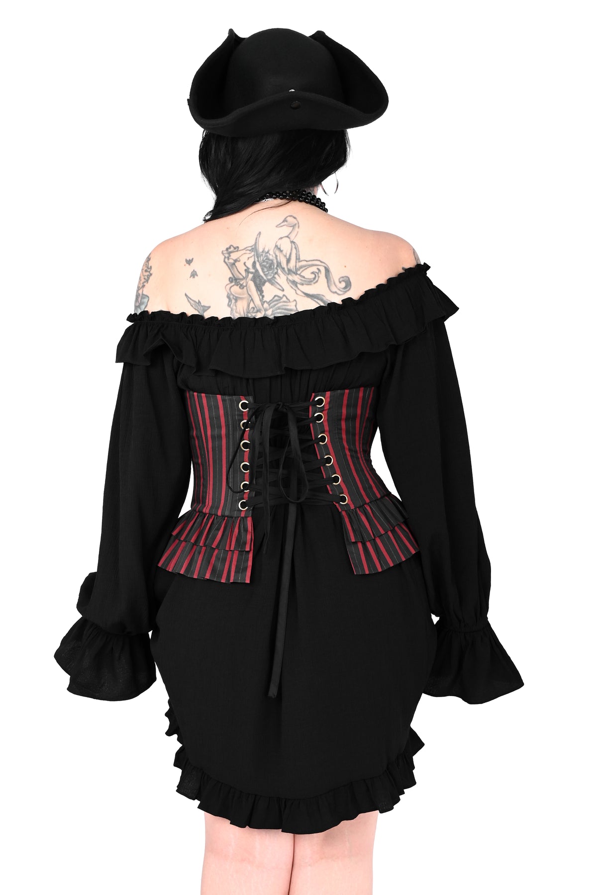 A model shown from the back wearing a black off-the-shoulder gothic dress with a red and black striped corset-style back panel, a black hat, and a black wig against a plain white background.