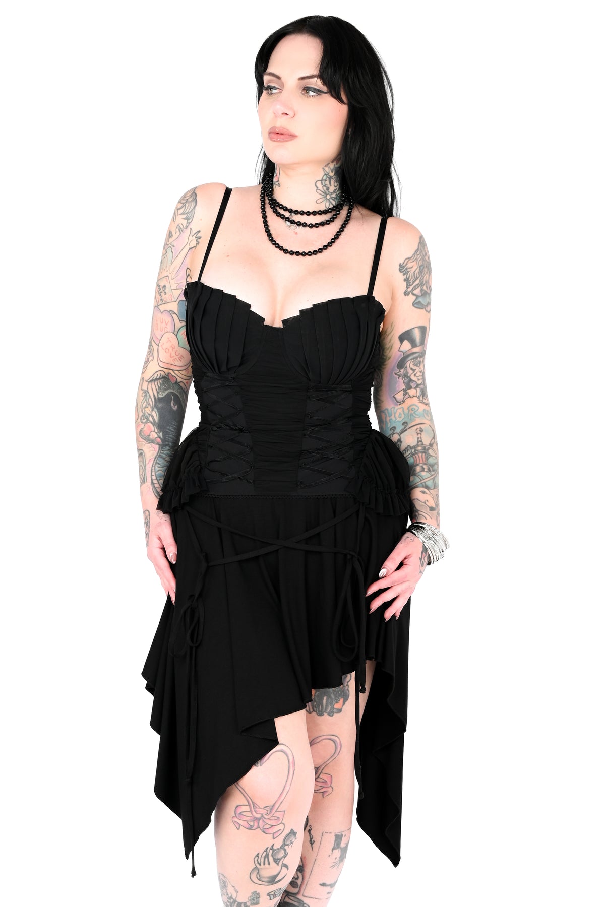 A model in a black asymmetrical high-low dress with a ruched corset-style bodice and thin shoulder straps, posed against a solid white background.