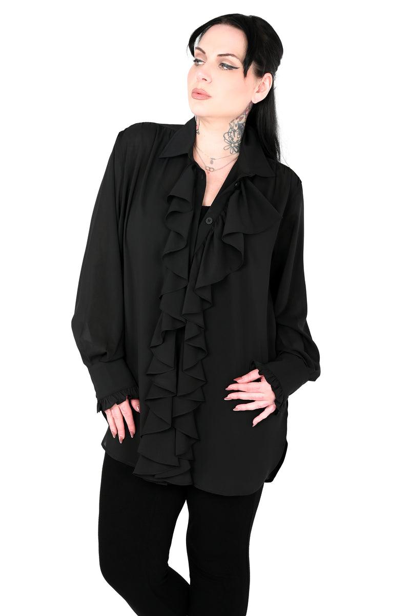A woman modeling a black long-sleeve blouse with dramatic cascading ruffles down the front, paired with black pants, against a plain white background.