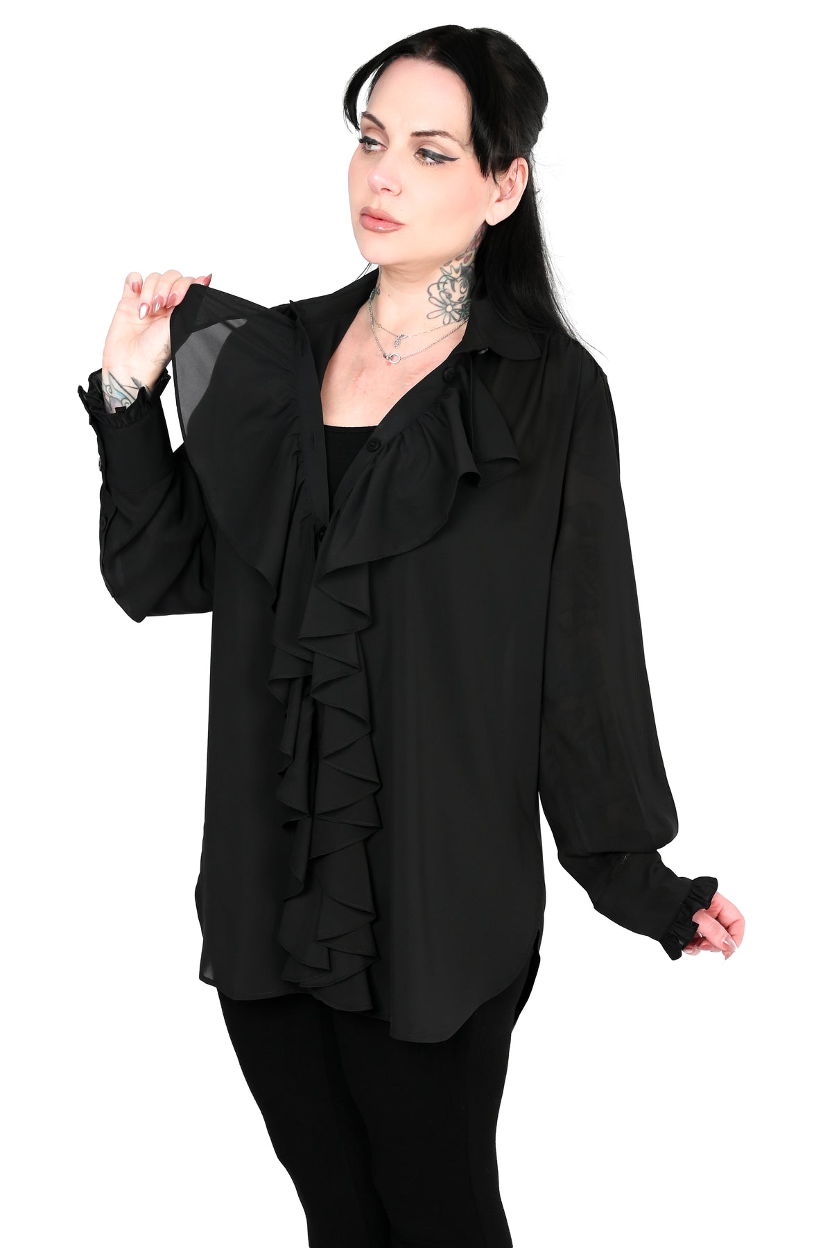 A woman modeling a black long-sleeve blouse with layered ruffle details along the front and collar, paired with black pants, against a plain white background.