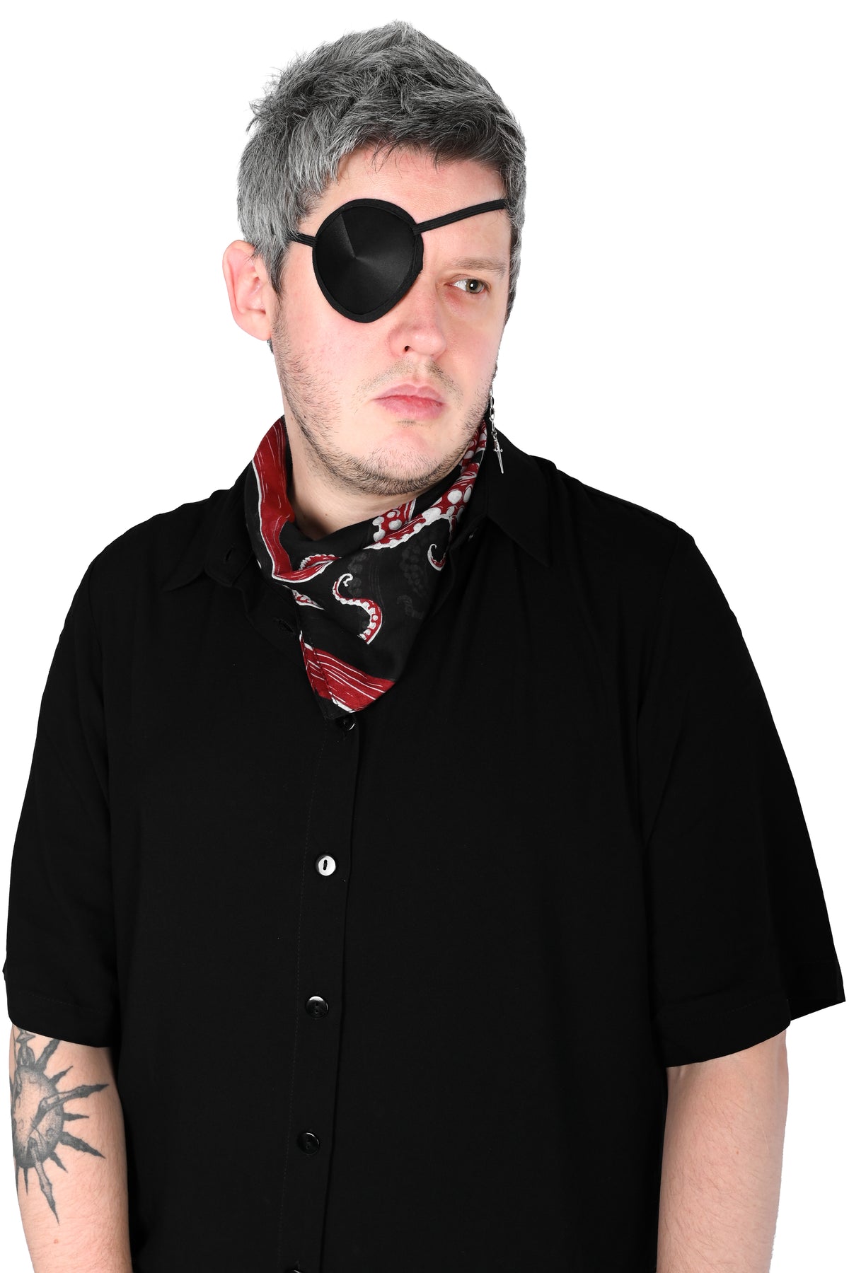 A man wearing a black eyepatch and a black short-sleeve button-up shirt showing off how to wear the Thar Be Monsters Scarf around his neck against a plain white background.
