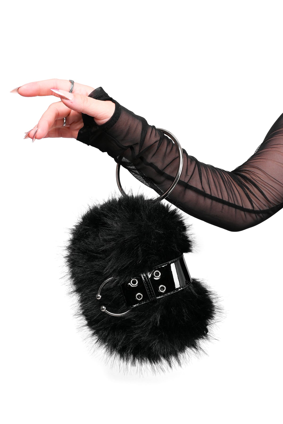 A black furry handbag with a giant metal O ring as a wristlet.The furry bag has a shiny pleather belt-like closure with a U ring/faux piercing at the end of it. The bag hands off the wrist of an arm sheer black long-sleeve against a plain white background.
