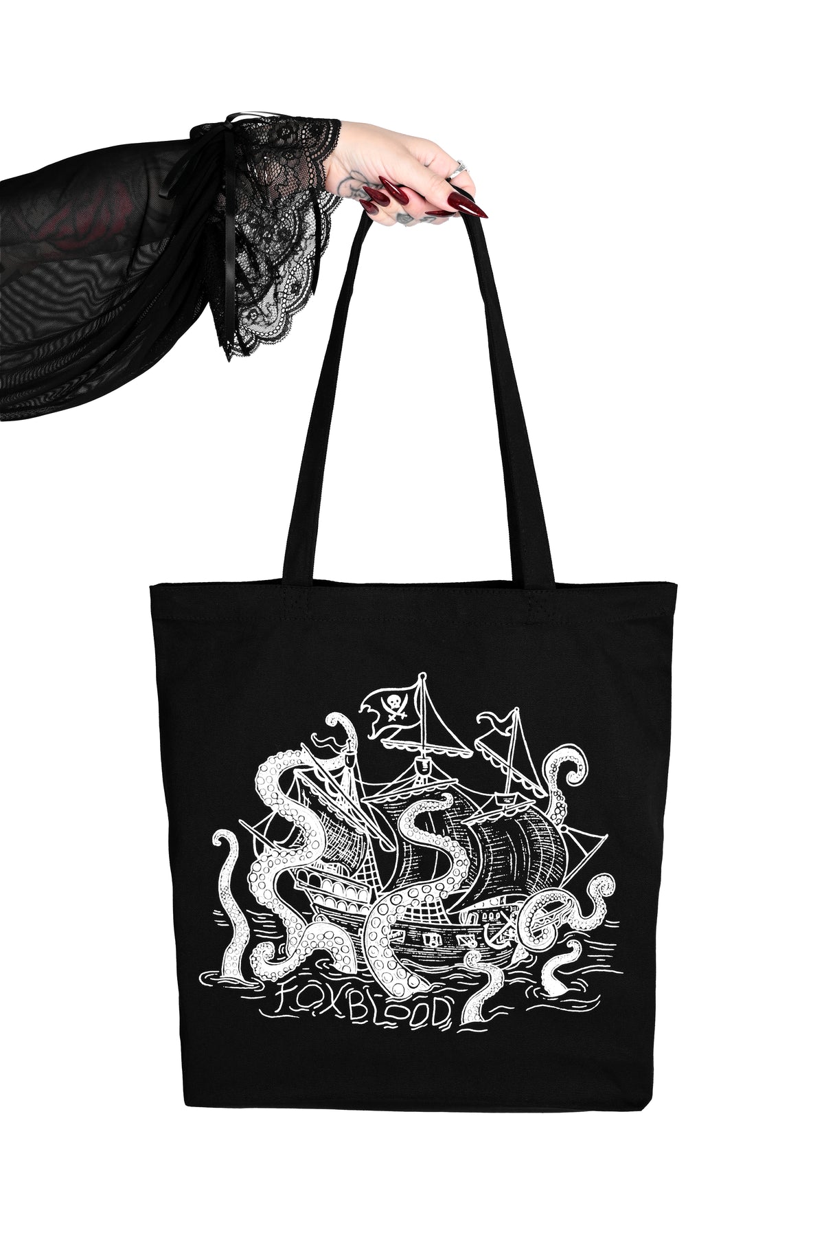 A arm is reaching out into the center of the image holding a black canvas tote bag. The bag features a sea monster/kraken attacking a pirate ship.