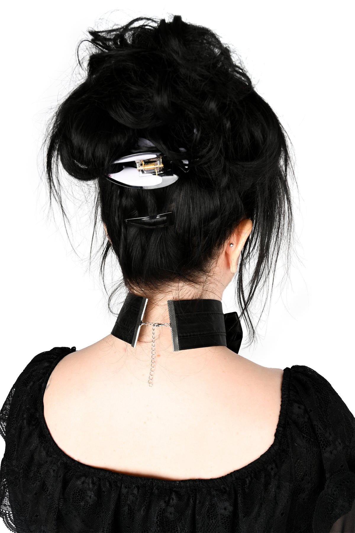 A person shown from the back wearing a black choker that secures with a small lobster clasp, styled with a messy black updo and a black hair clip against a white background.