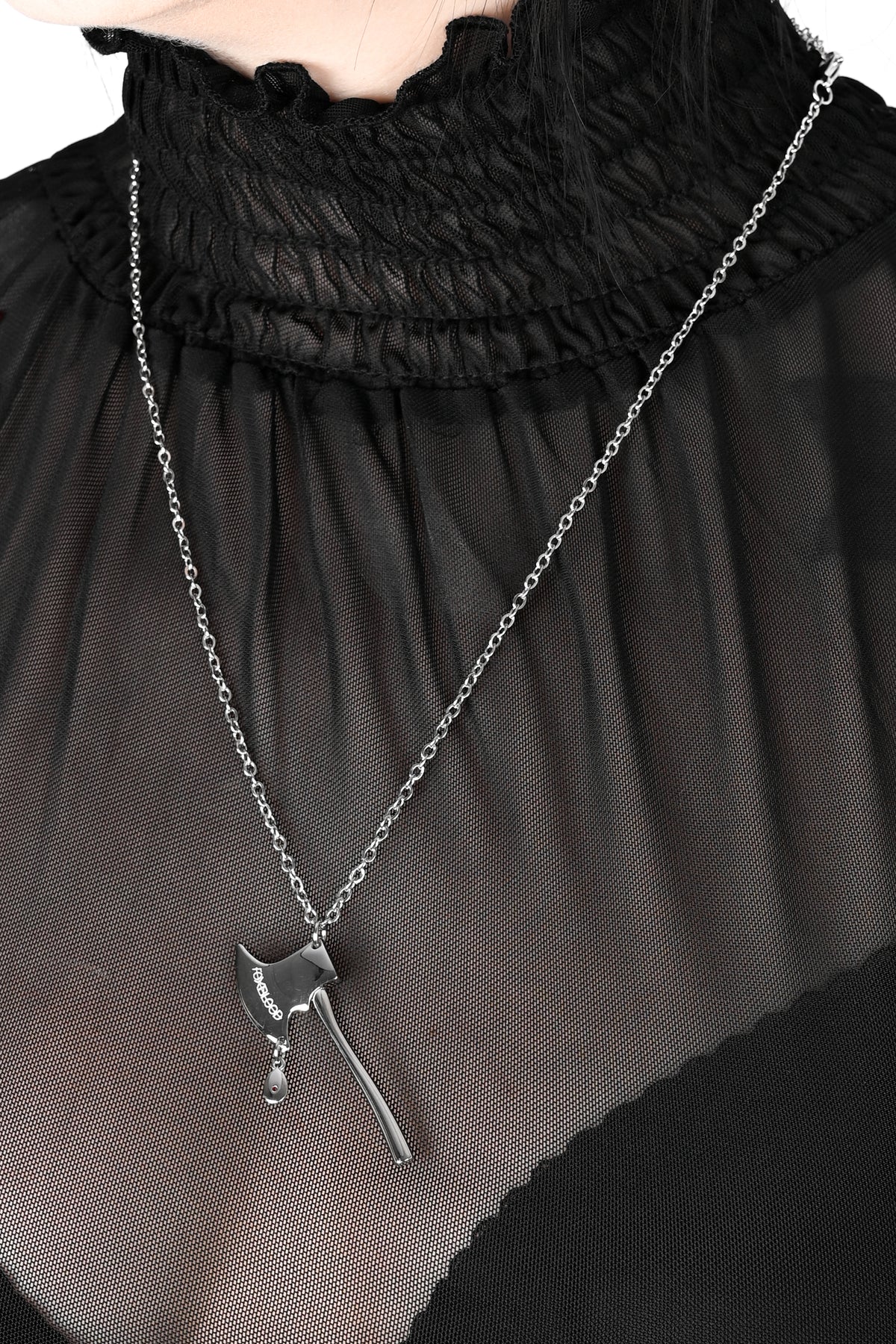 A silver-toned axe pendant necklace worn by a model in a sheer black ruffled top.