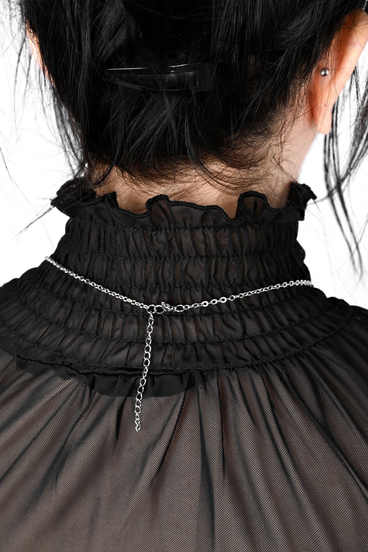 A close-up back view of a person wearing a black smocked blouse with a delicate silver chain accessory tied around the neck.