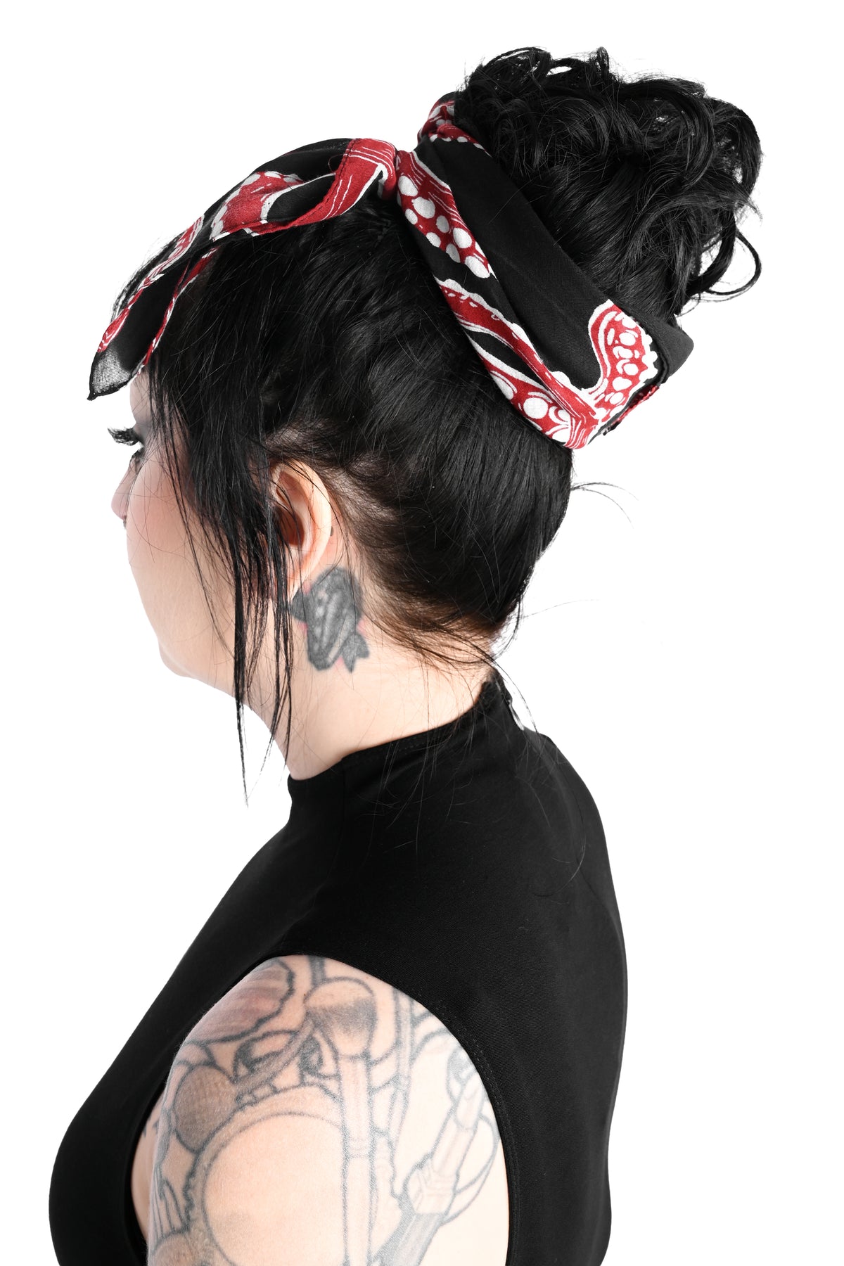 A back facing side view of a model dressed in all black wearing the thar be monsters scarf wrapped around her head. The scarf is black with red and white tentacles all over.  Shot on a white background.
