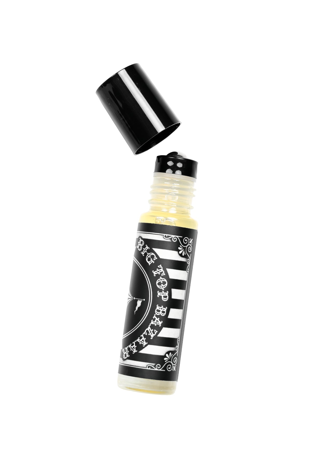 A glass roll on perfume bottle with its cap off, floating diagonally on a solid white background. The bottle contains a perfume oil and the sticker on the bottle features a black and white striped label with the text "BIG TOP BAZAAR"