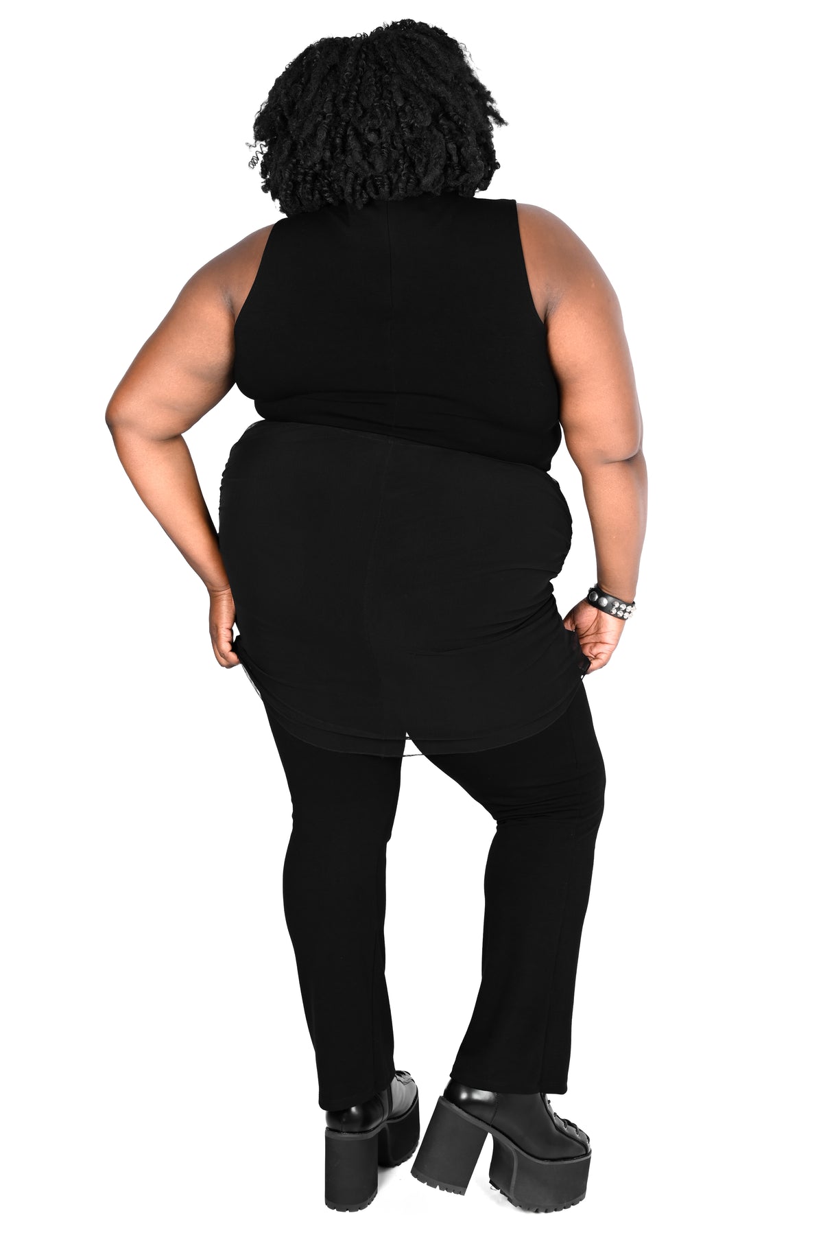 A plus-size model shown from the back wearing a black sleeveless top, black pants, and black platform heels against a plain white background.