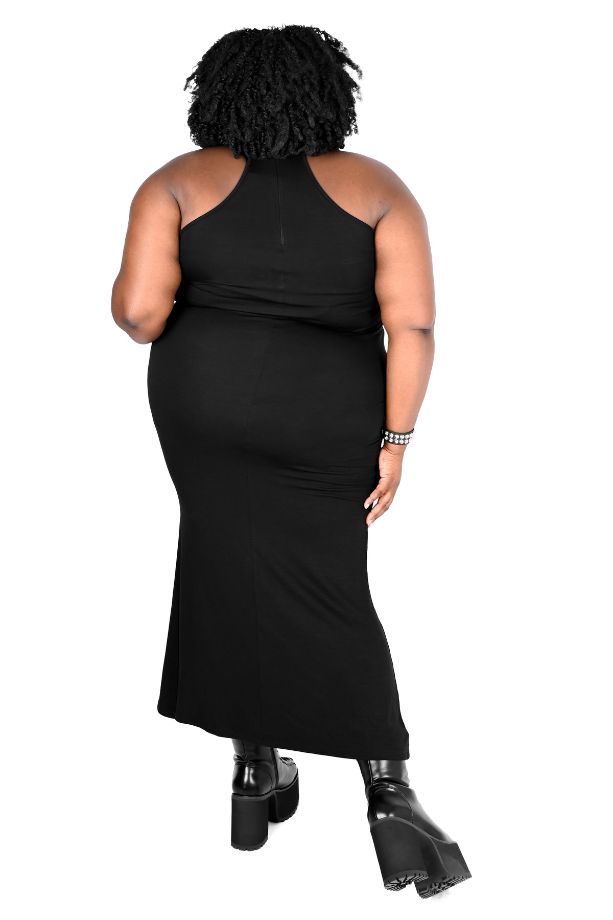 A plus size model shown from the back wearing a black halter-neck maxi dress and black platform boots against a plain white background.