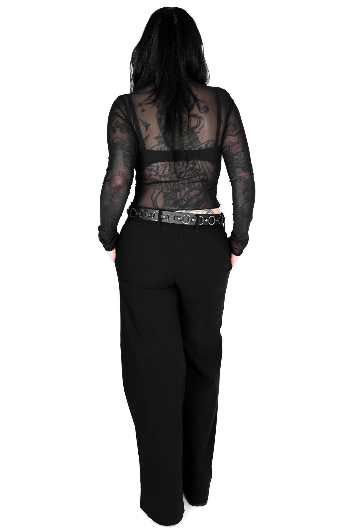 A model shown from the back wearing a black sheer long-sleeve top with a lace-up back and black wide-leg trousers, set against a plain white background.